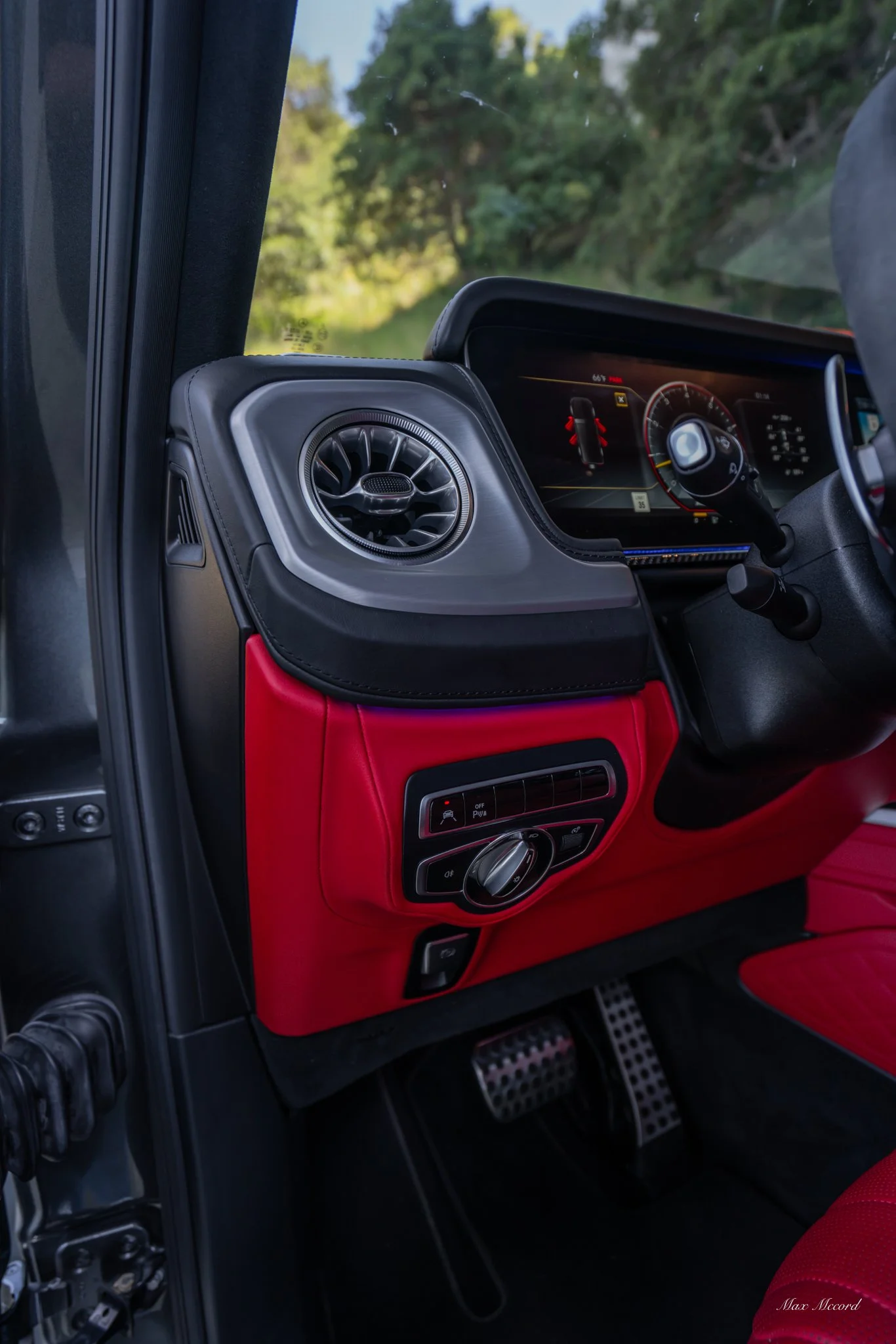 Close-up of a vehicle's dashboard with a digital display, air vent, and control switches, featuring red and black interior accents.