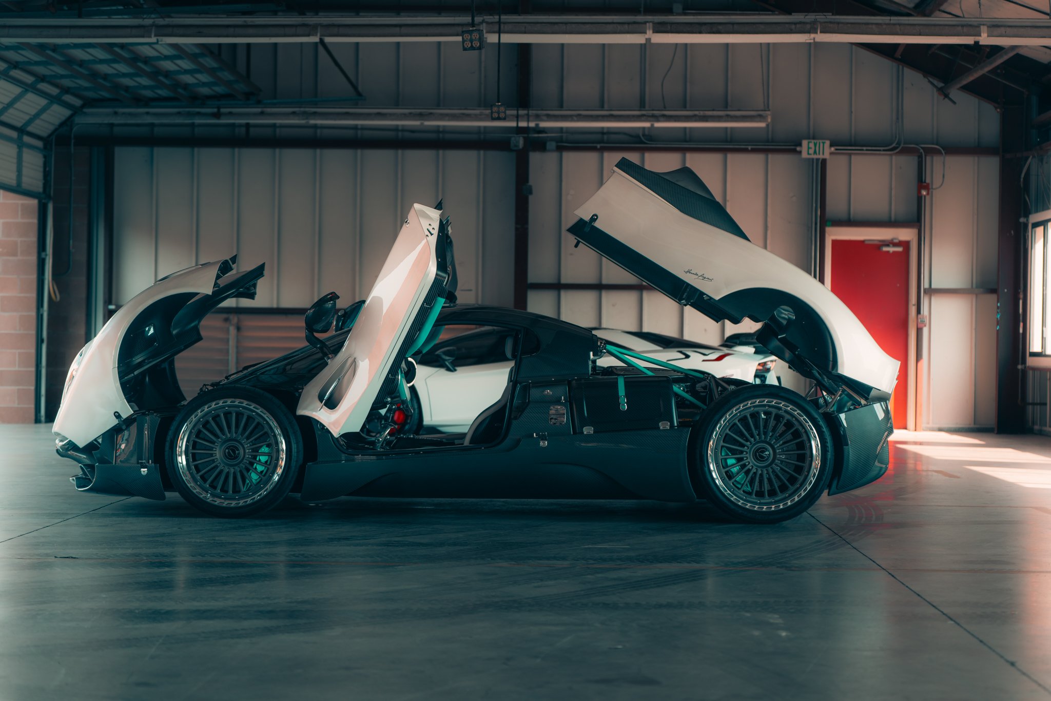 A white sports car with gull-wing doors open inside a garage.