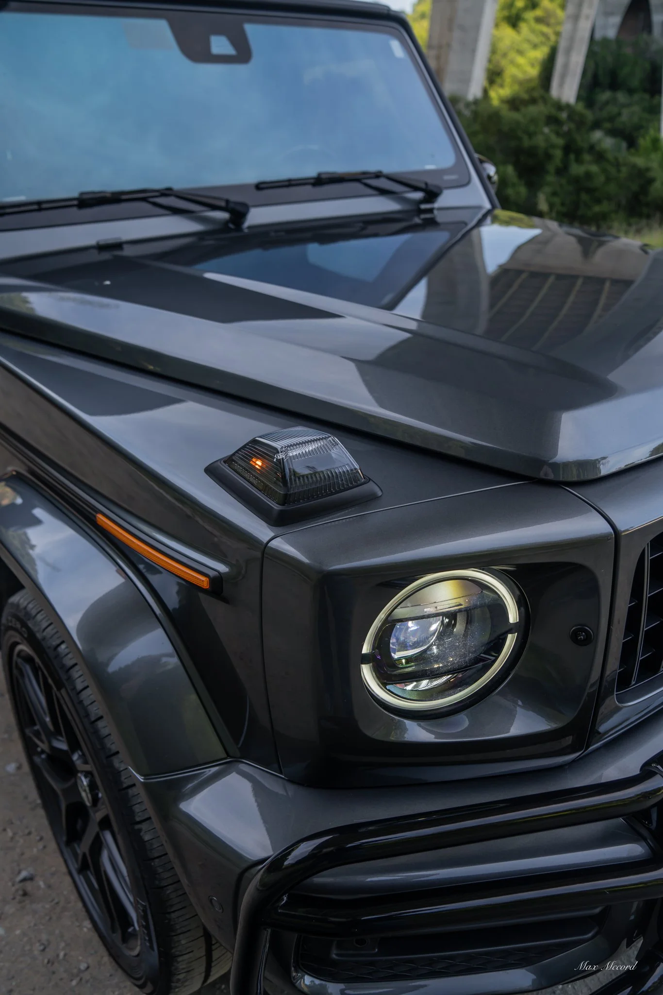 Close-up of a black luxury SUV, showing the front right headlight with LED ring, the round turn signal indicator on the hood, and a black bull bar on the bumper.