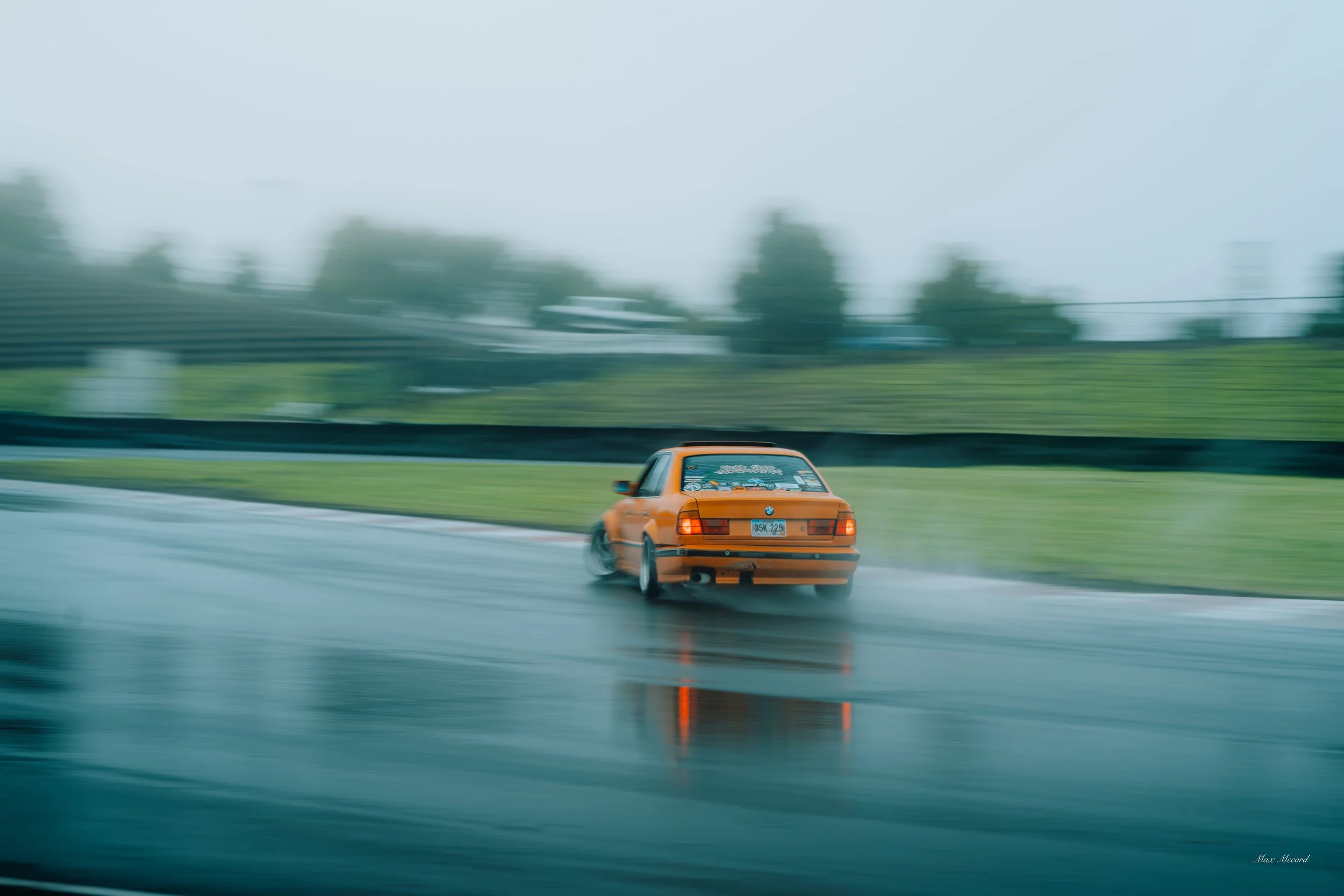 Orange car driving on a wet racetrack on a rainy day with blurred motion and background