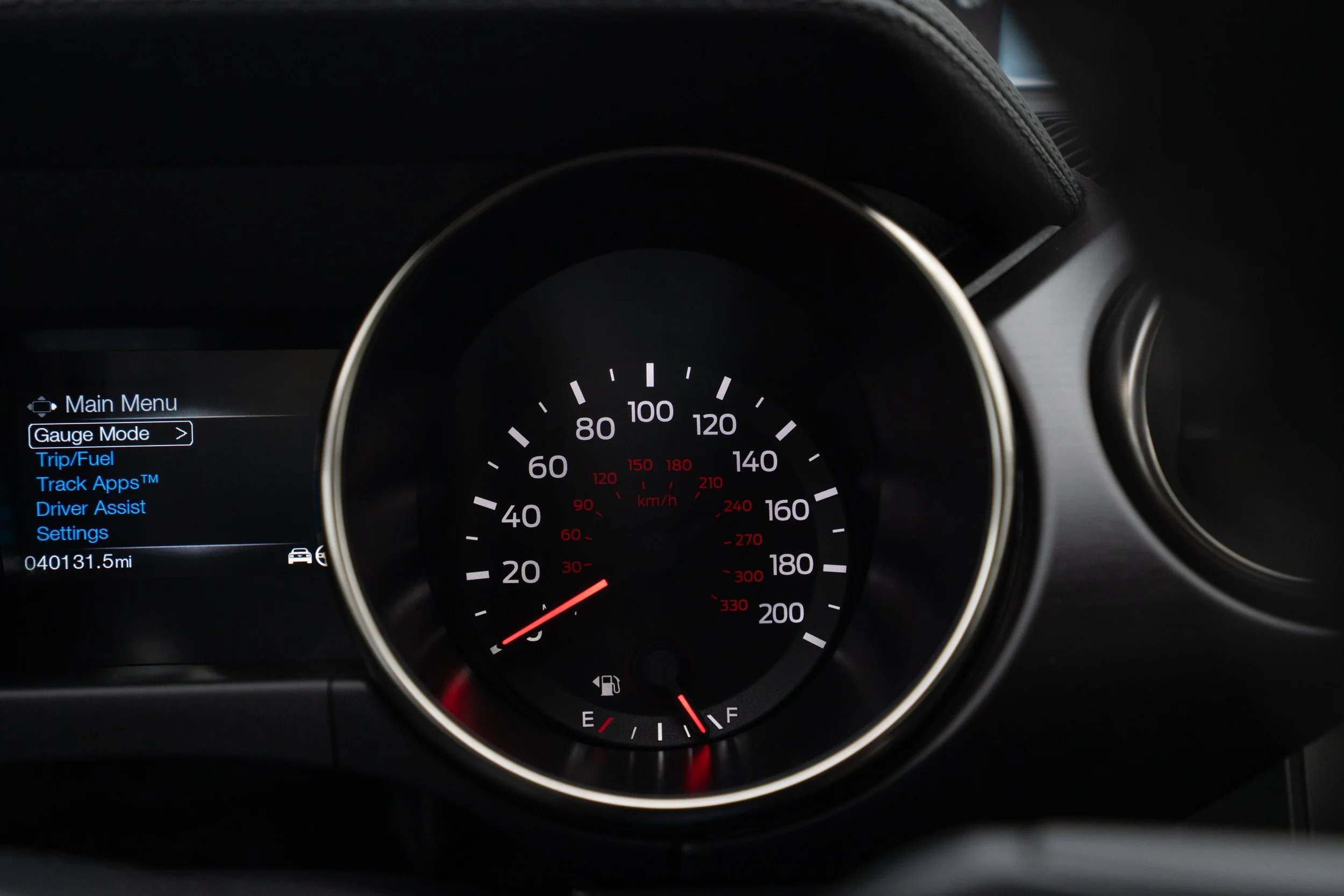 Car dashboard showing speedometer, fuel gauge, and a digital screen with menu options including Gauge Mode, Trip/Fuel, Track Apps™, Driver Assist, and Settings.