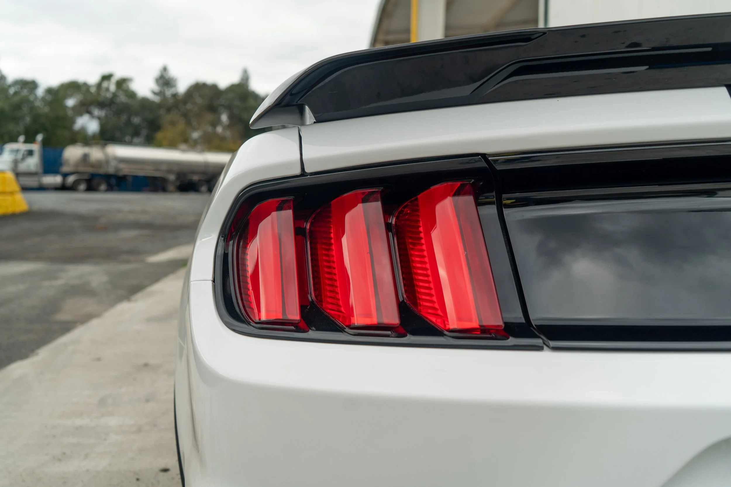 Close-up of the rear of a white sports car, showing its red tail lights and black trim.