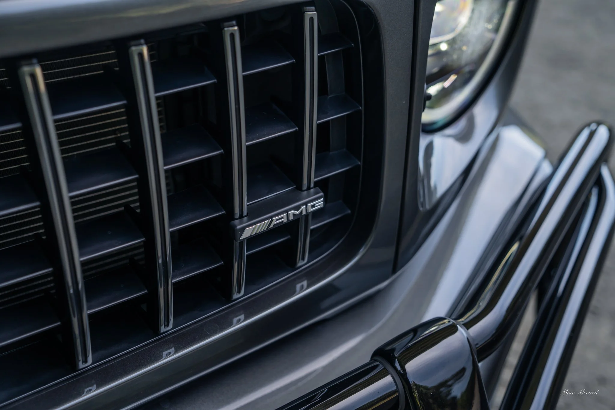 Close-up of the front grille of a black luxury AMG Mercedes-Benz vehicle, featuring vertical chrome slats and the AMG badge.