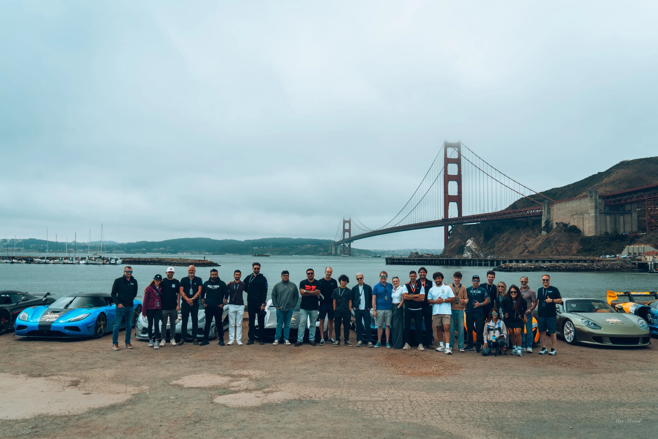 Group of people standing in front of luxury cars with Golden Gate Bridge in the background.