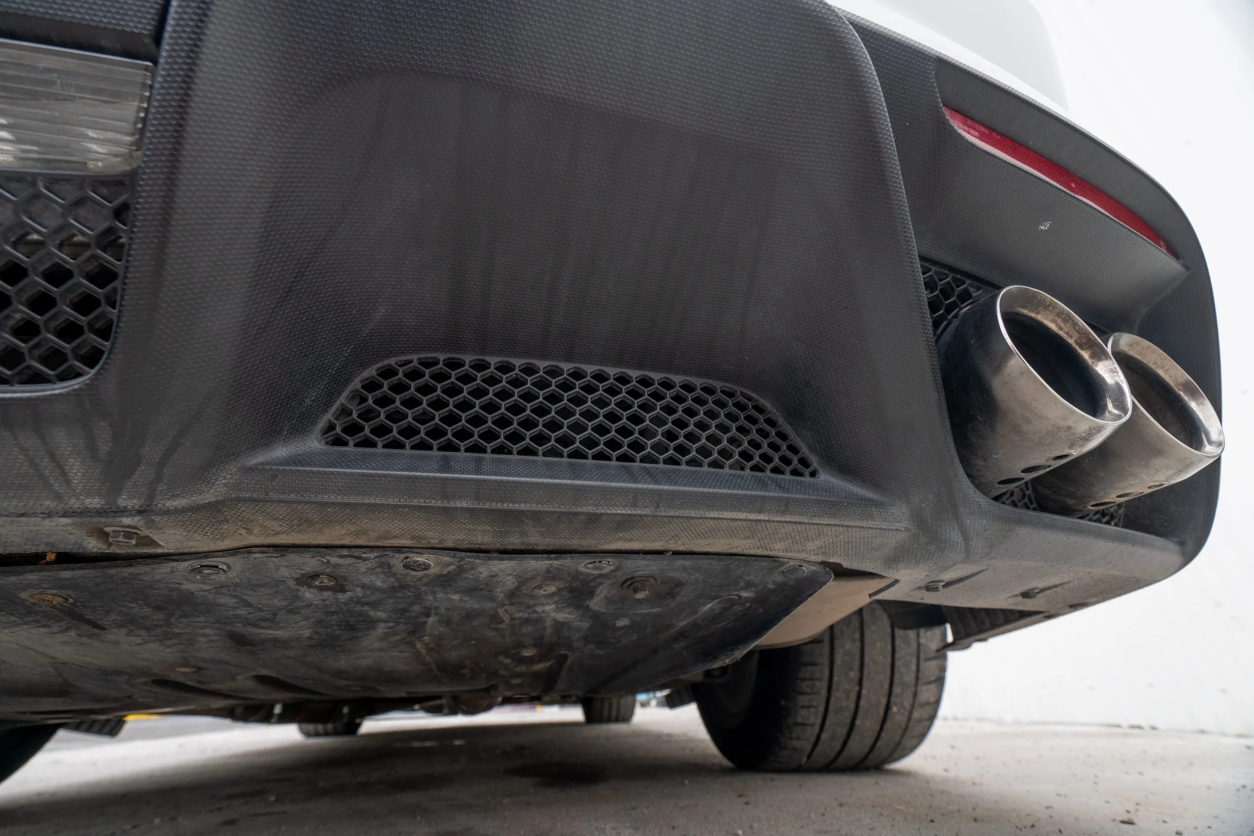 Close-up of the rear underside of a sports car showing dual exhaust pipes, rear diffuser, and tire.