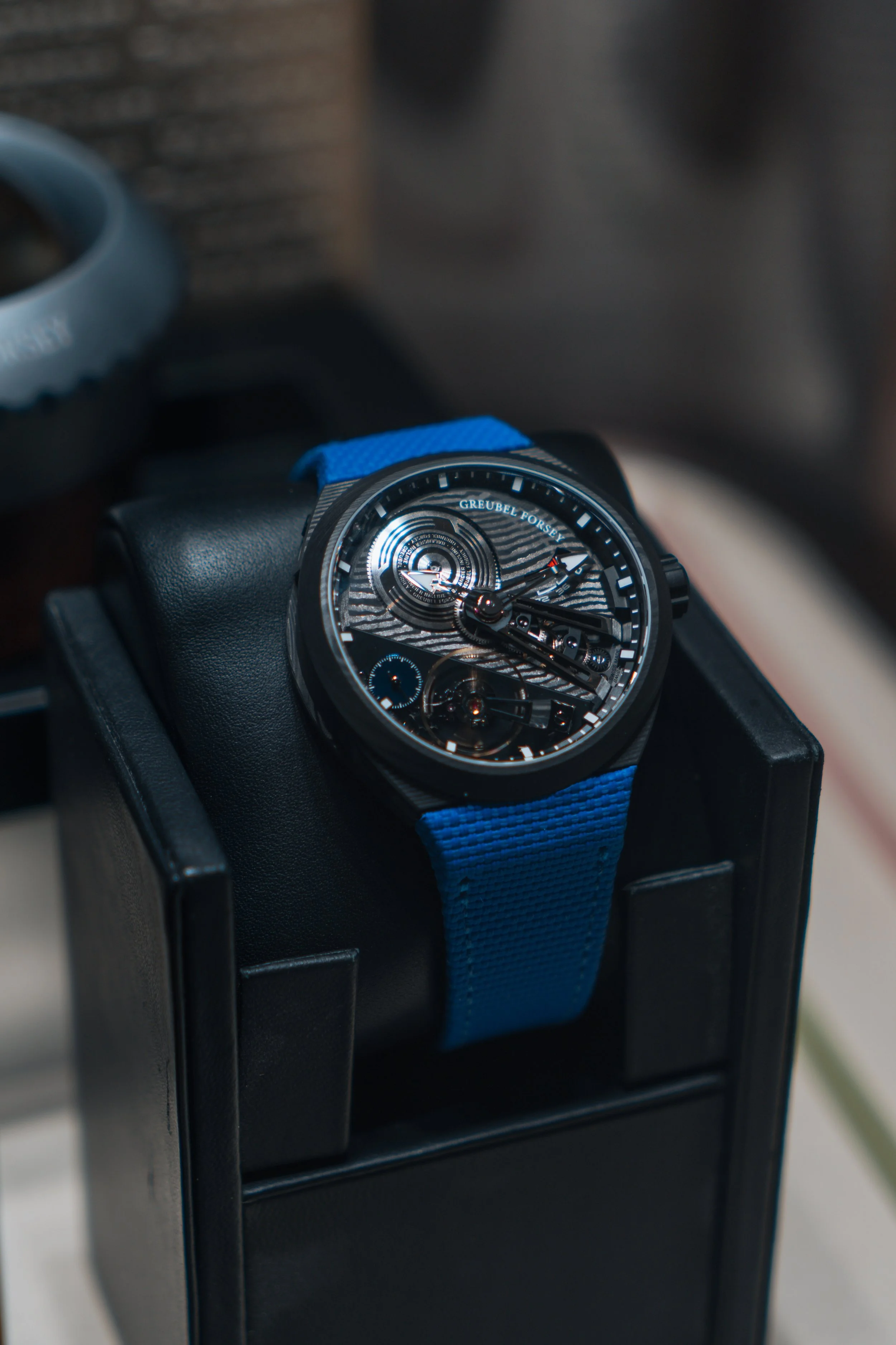 A black and blue wristwatch with a textured dial on a black display stand.