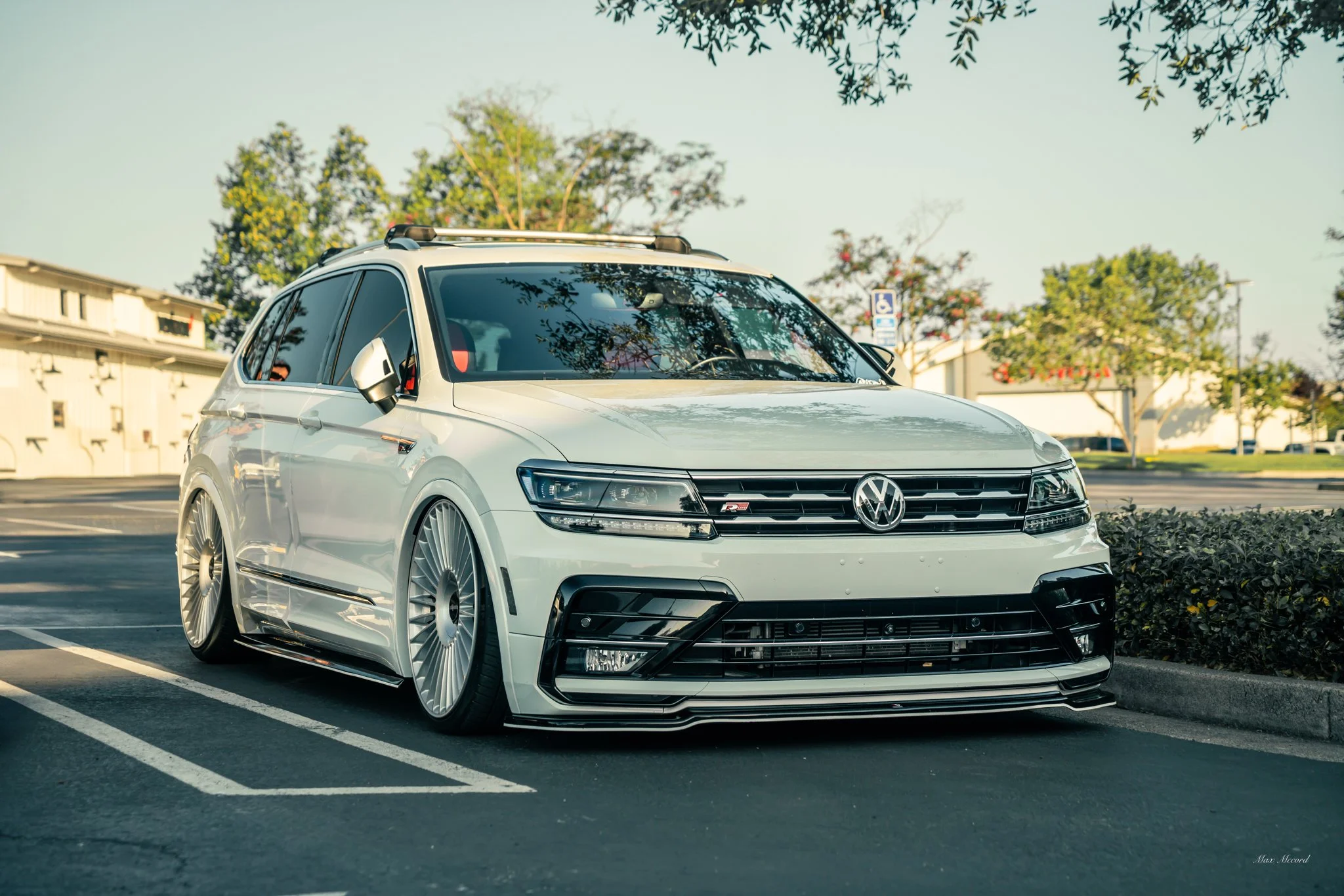 A white Volkswagen sedan with custom wheels parked in a parking lot.