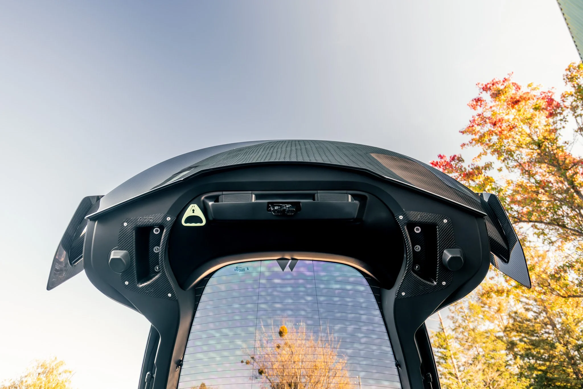 Close-up of a futuristic robot or vehicle with a transparent screen reflecting autumn trees and sky, set outdoors.