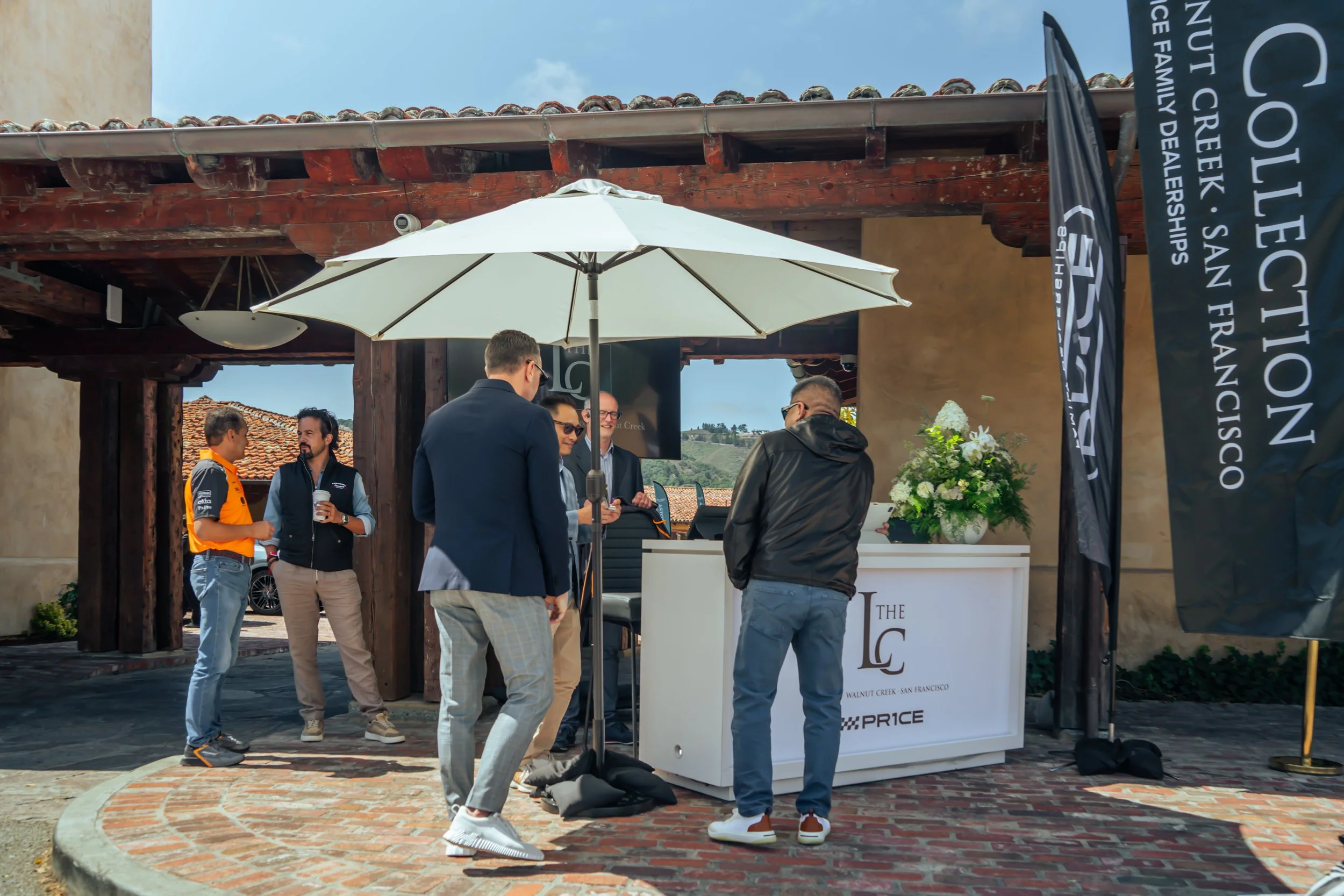 Group of people gathered around a booth with a sign for Walnut Creek, San Francisco, at an outdoor event, with an umbrella and banners visible.