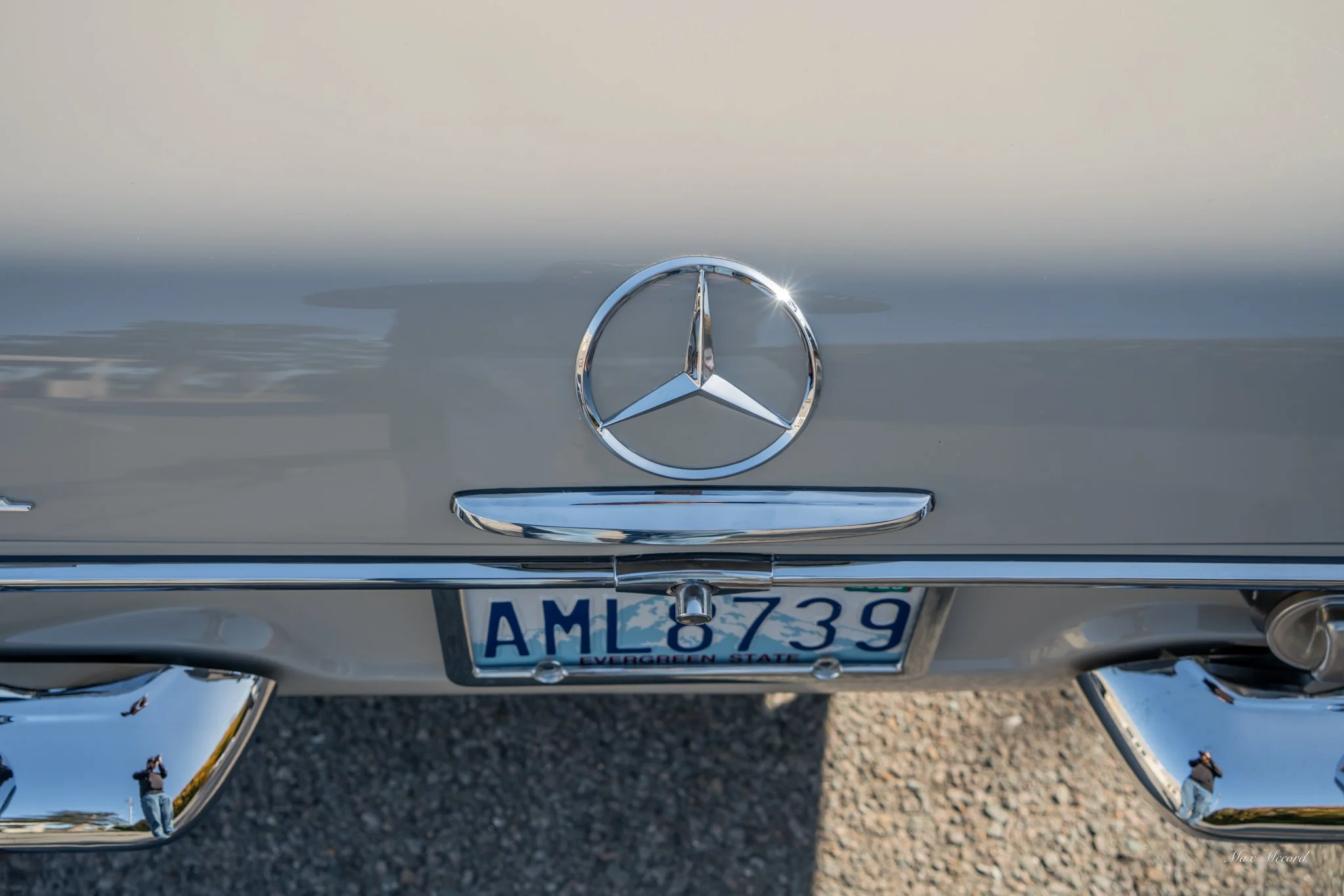 Close-up of the rear of a silver Mercedes-Benz car showing the Mercedes logo, a license plate reading AML 7339 from Virginia, and chrome bumper details.