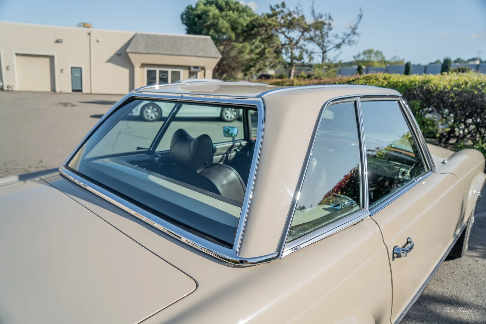A beige vintage car parked outside with a building and trees in the background.