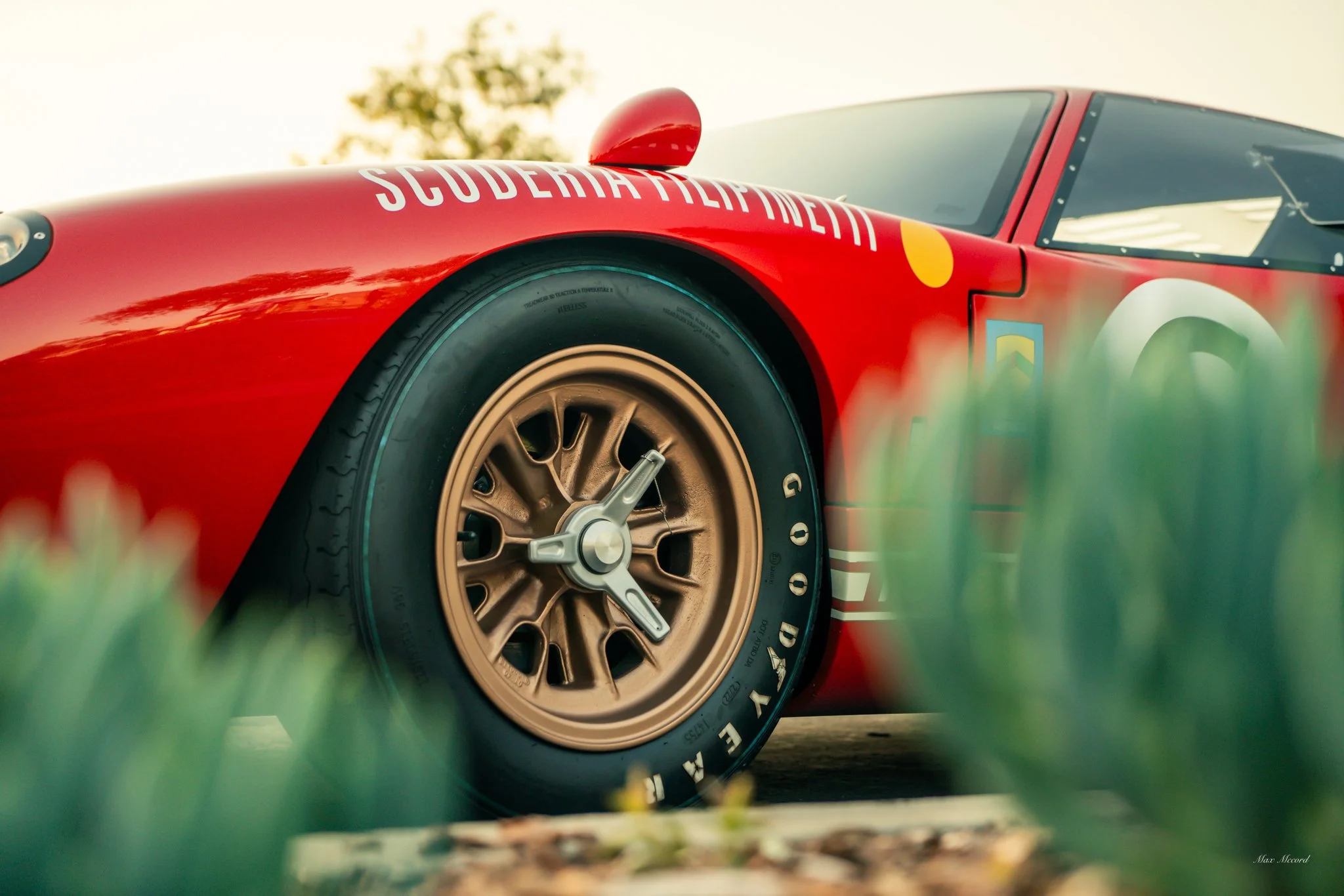 Close-up of a red vintage race car with gold wheel rims, the words 'SUBDERMATOPHORE' written on the top edge, and a partially obscured number on the side.