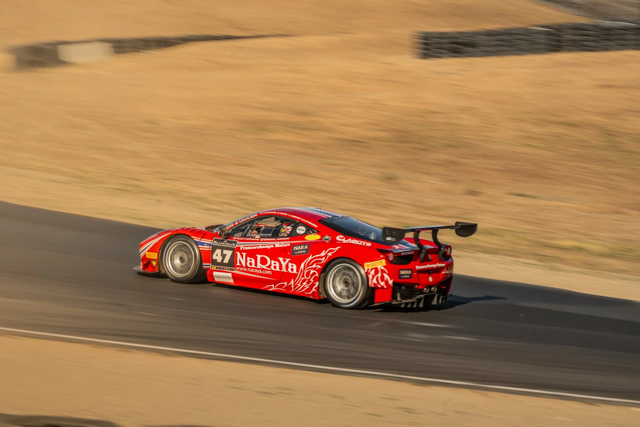 A red race car speeding on a race track with a desert landscape in the background.