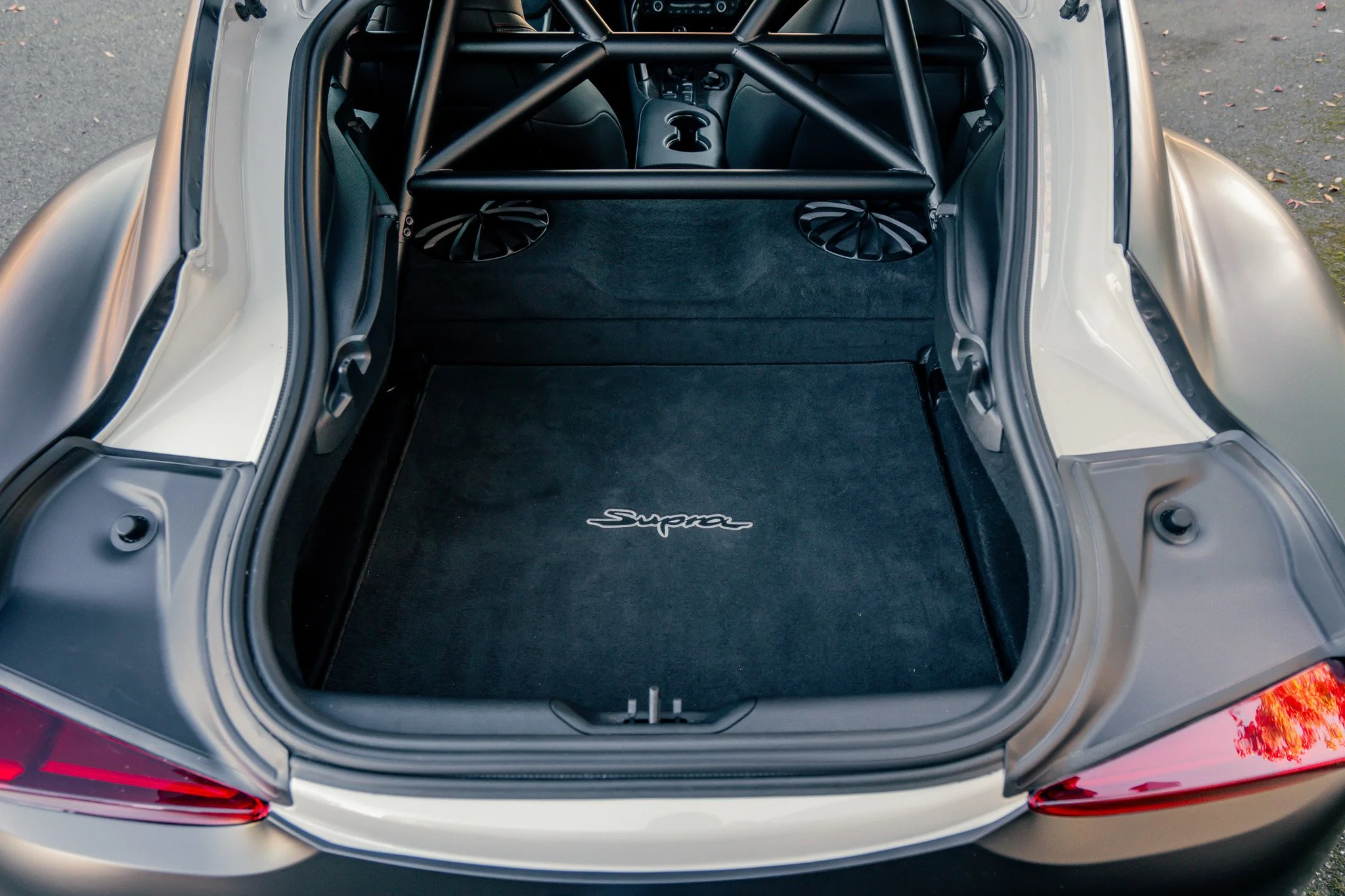 The rear trunk of a sports car with a custom black carpeted floor mat that has the word 'Supra' embroidered on it.