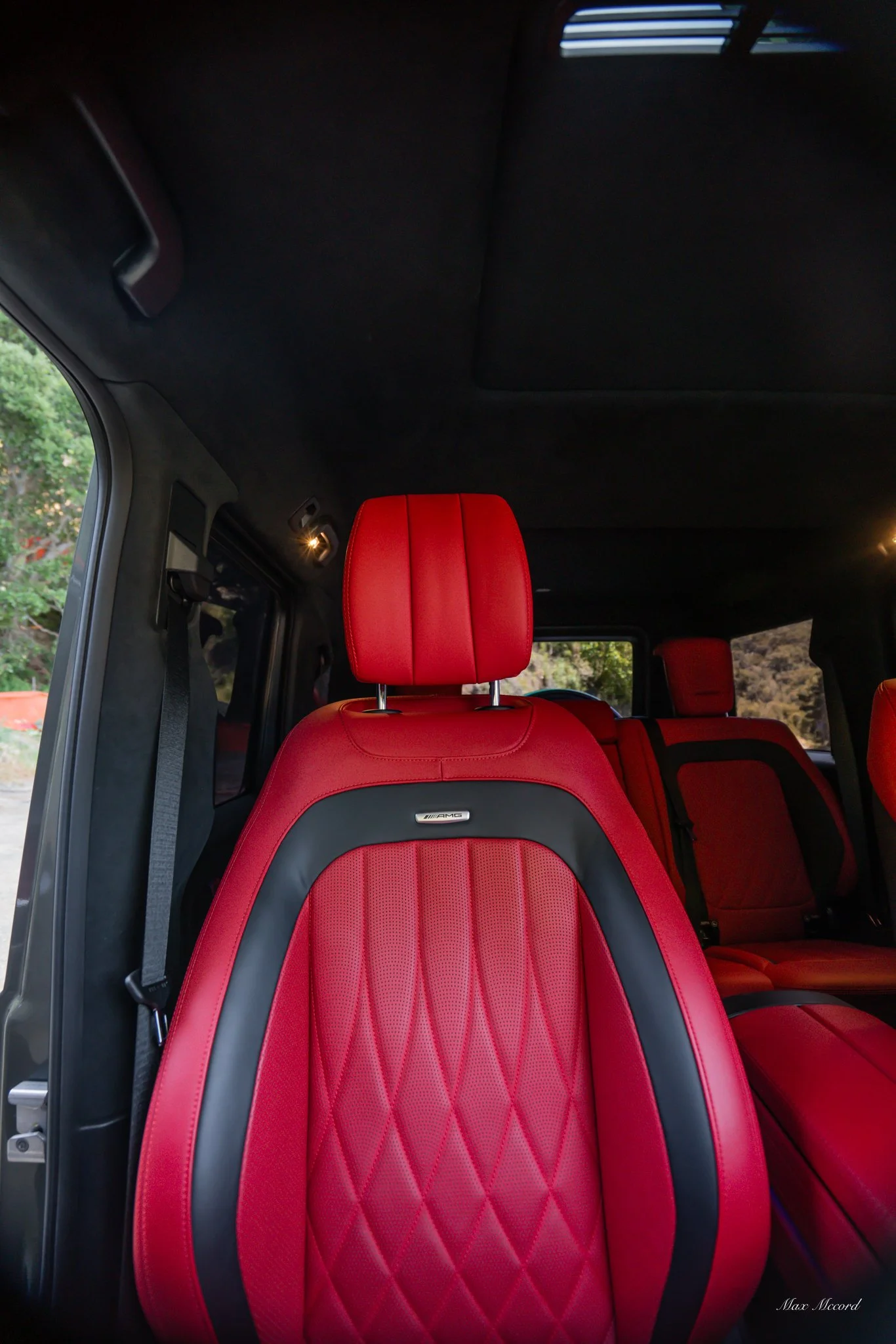 Interior of a luxury car with red leather seats and black accents, featuring the front seat with diamond stitching, headrest, and headliner.