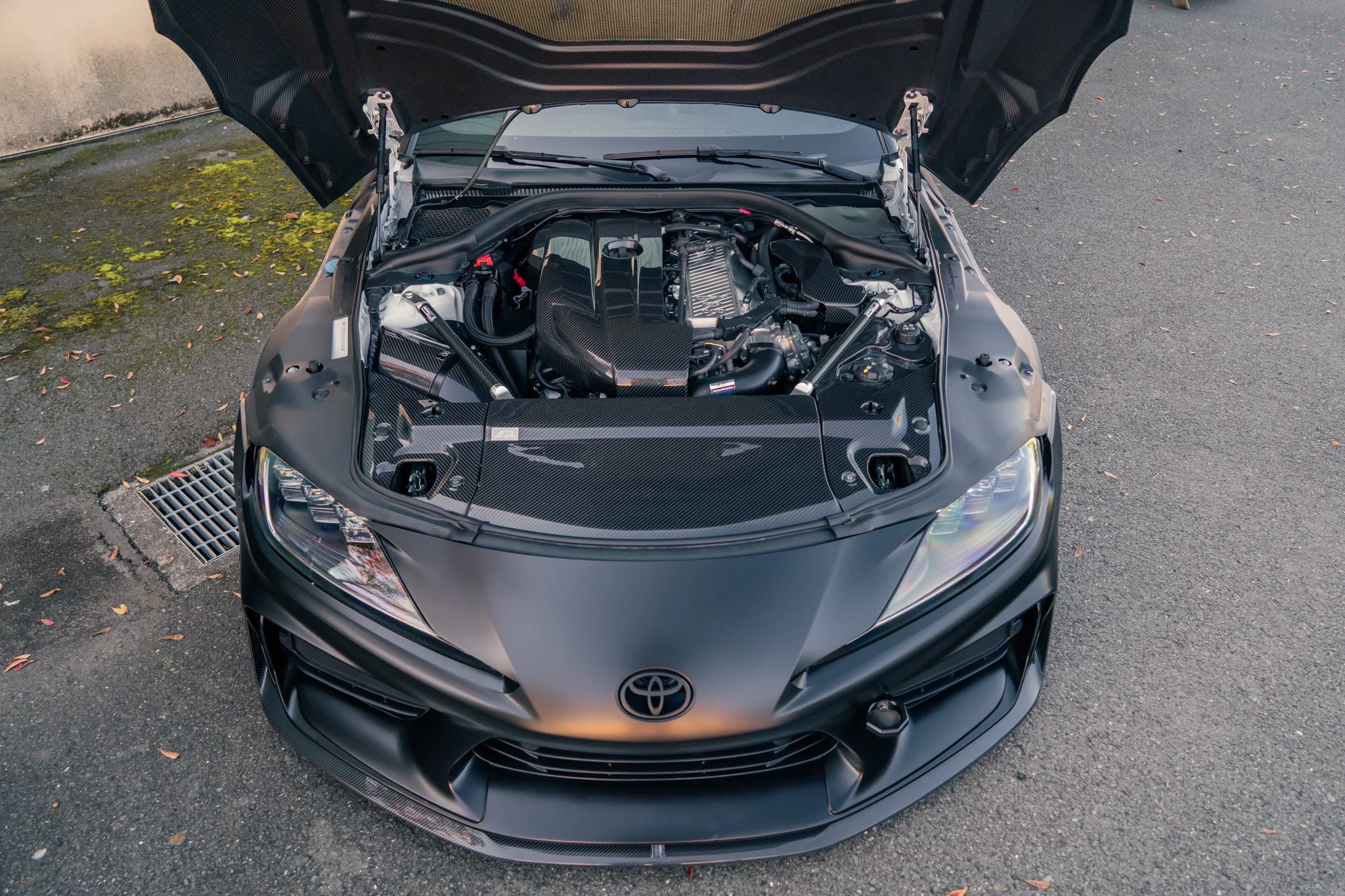 Front of a black Toyota sports car with hood open revealing a high-performance engine, carbon fiber accents, and aerodynamic design.