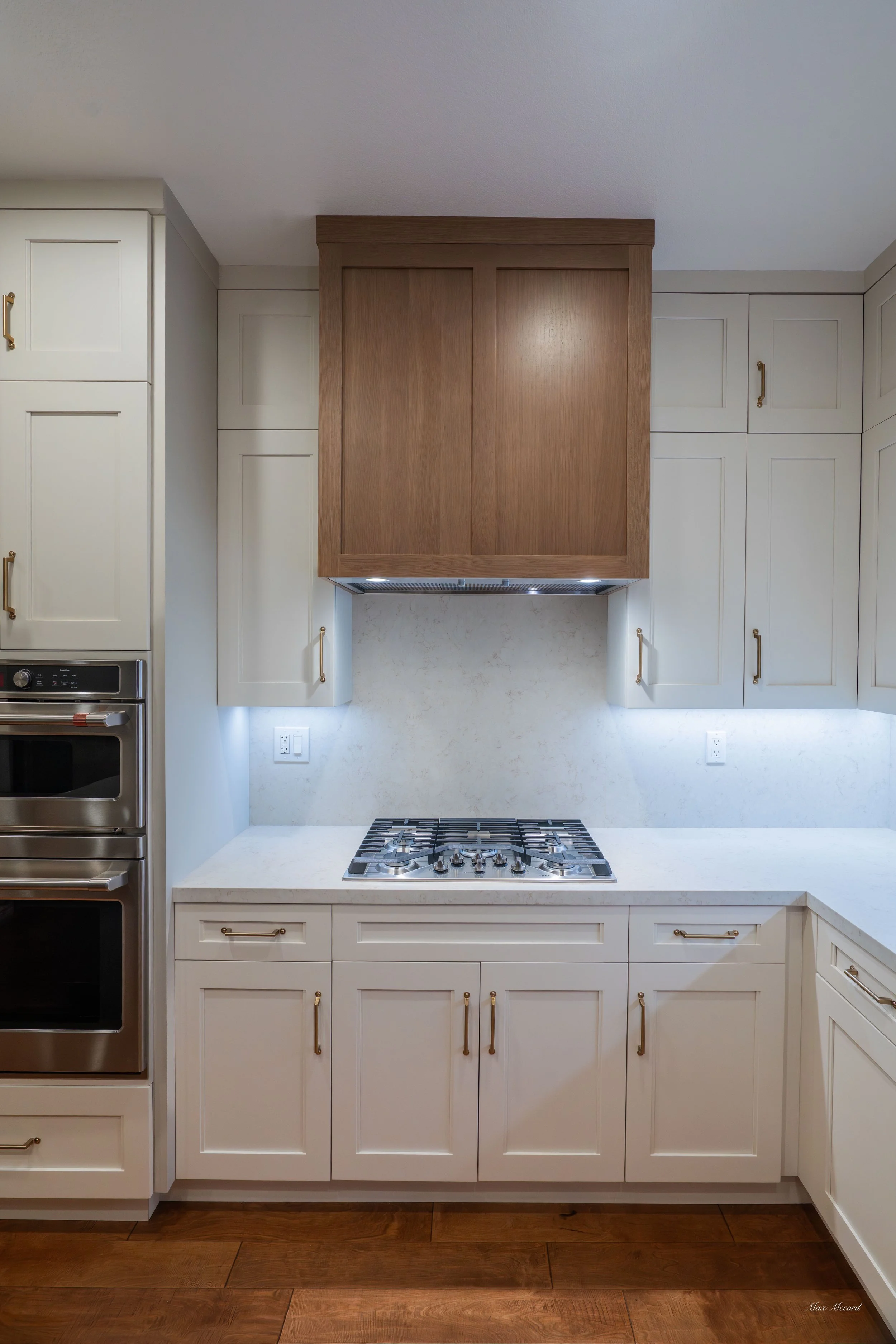 Kitchen with white cabinets, a gas stove, stainless steel oven, and wooden floors.