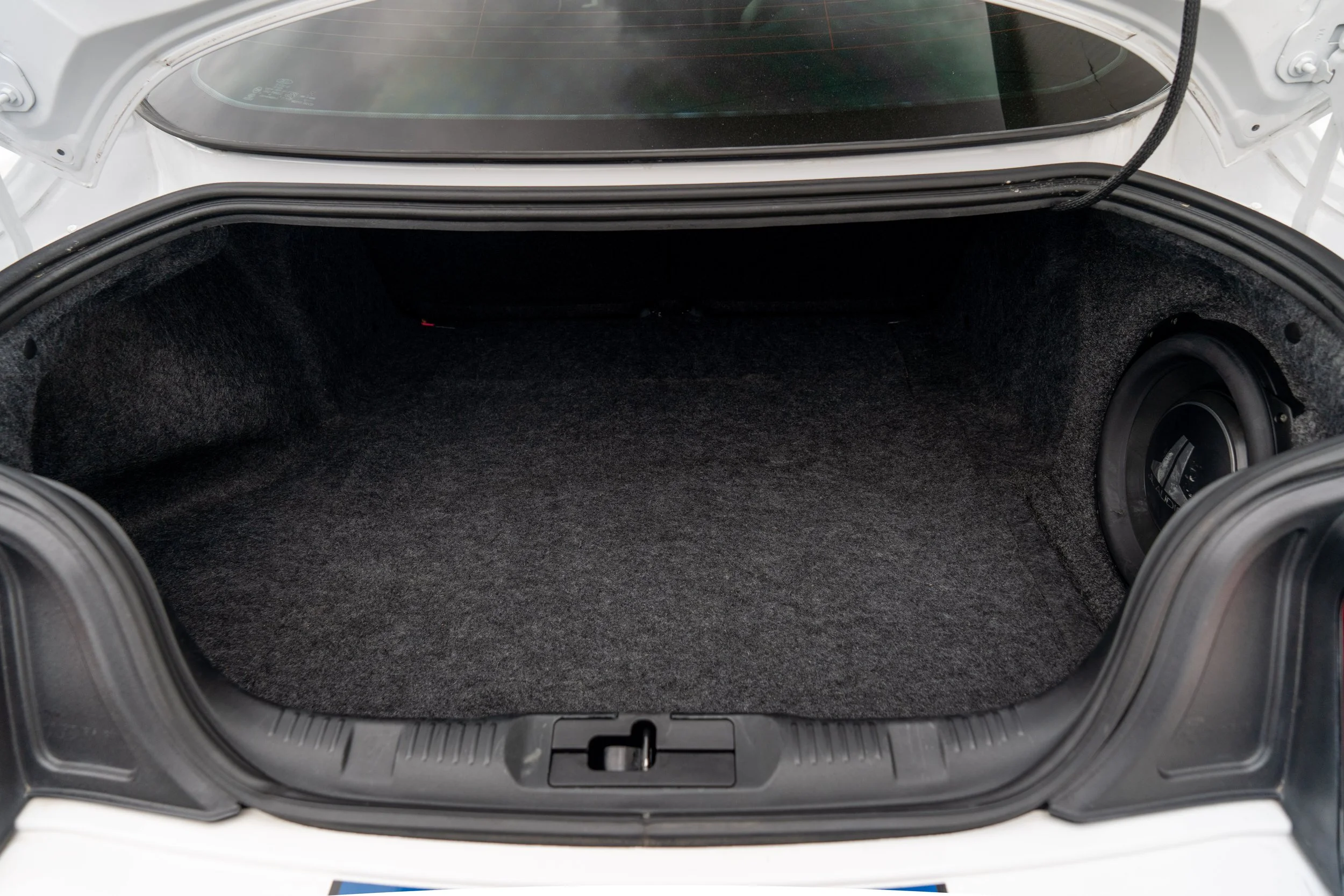 Empty car trunk with black carpeting and a speaker in the right corner.