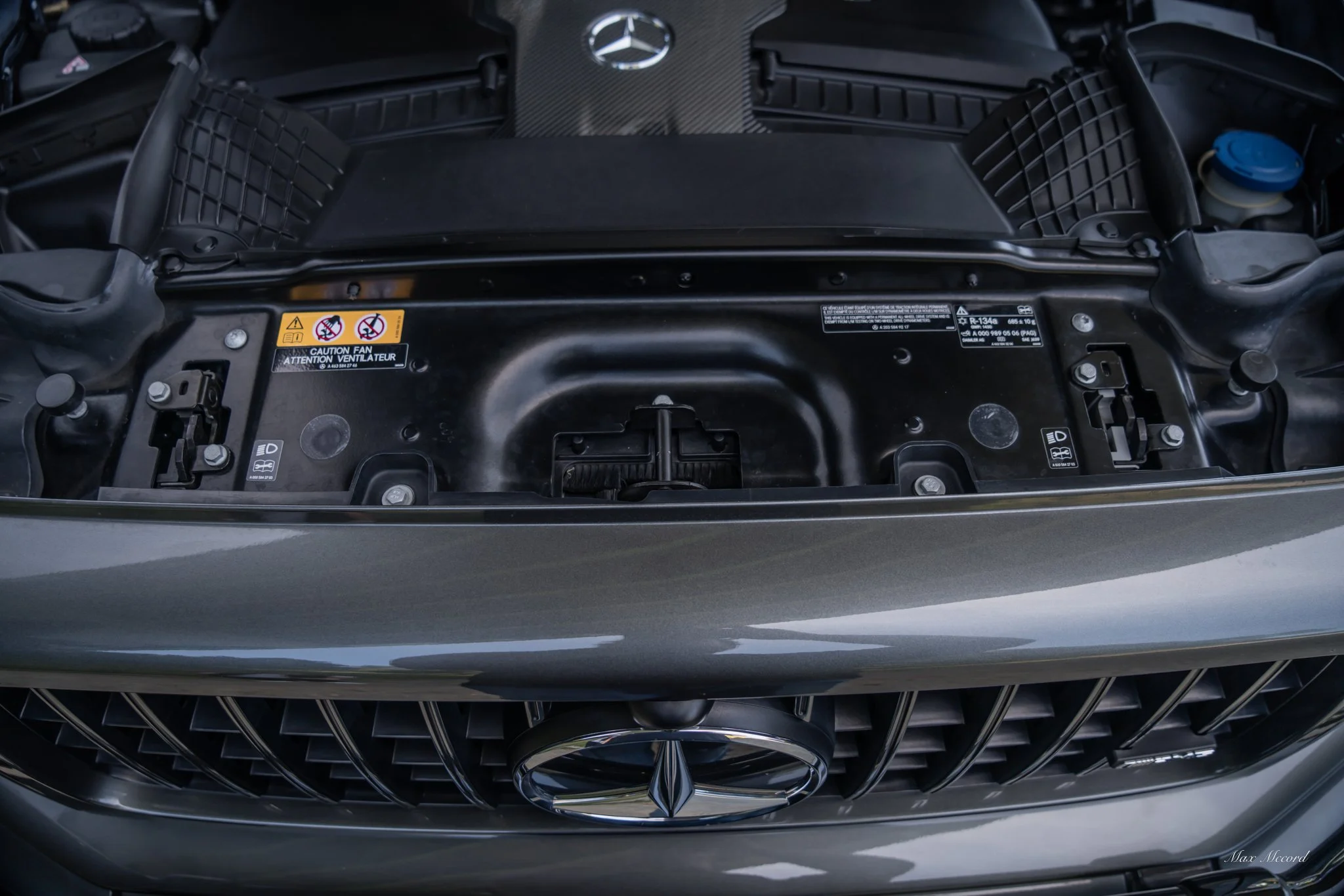 Front of a Mercedes-Benz car with the hood open, showing the engine compartment and grille with the Mercedes-Benz logo.