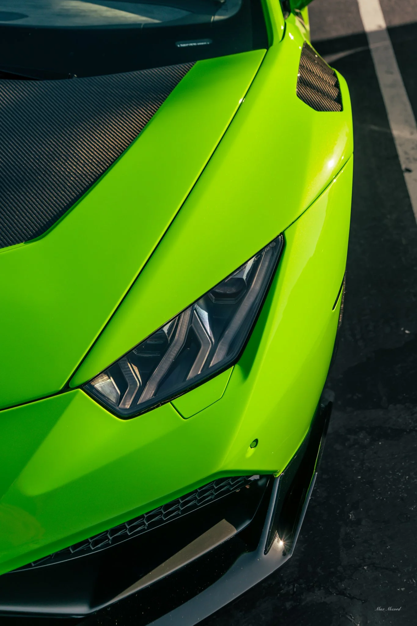 Close-up of a bright green sports car showing the front left headlight, vent details, and hood with black accents.