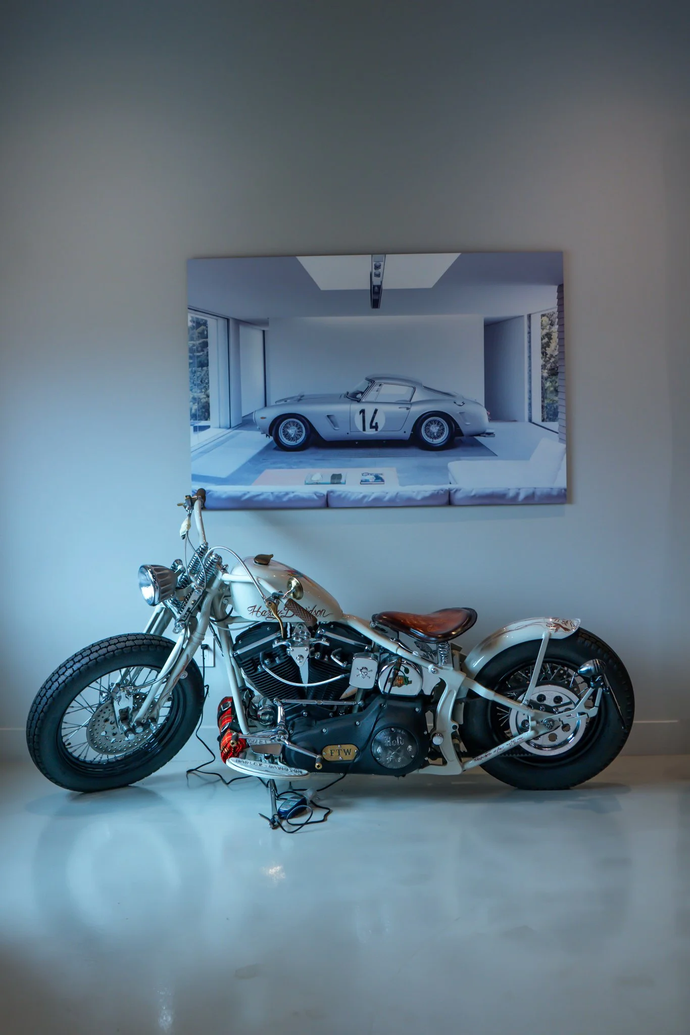 A vintage Harley Davidson motorcycle in front of a large framed poster of a classic race car.