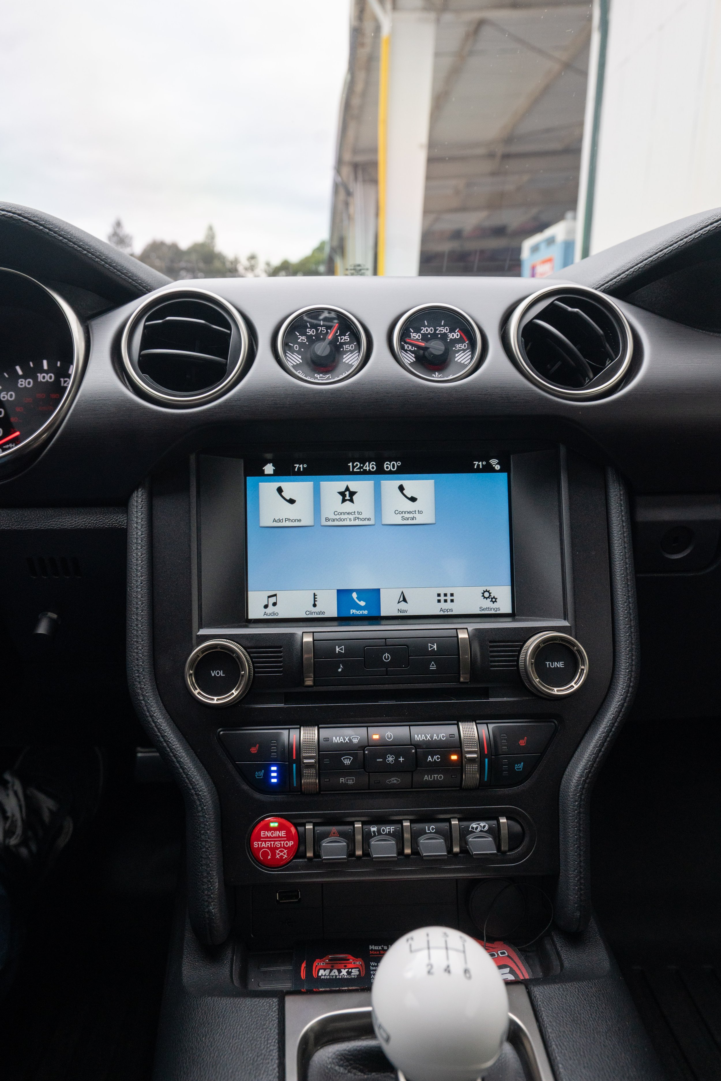 Interior view of a car dashboard showing air vents, gauges, touchscreen display, and control buttons, with a gear shift in the foreground.