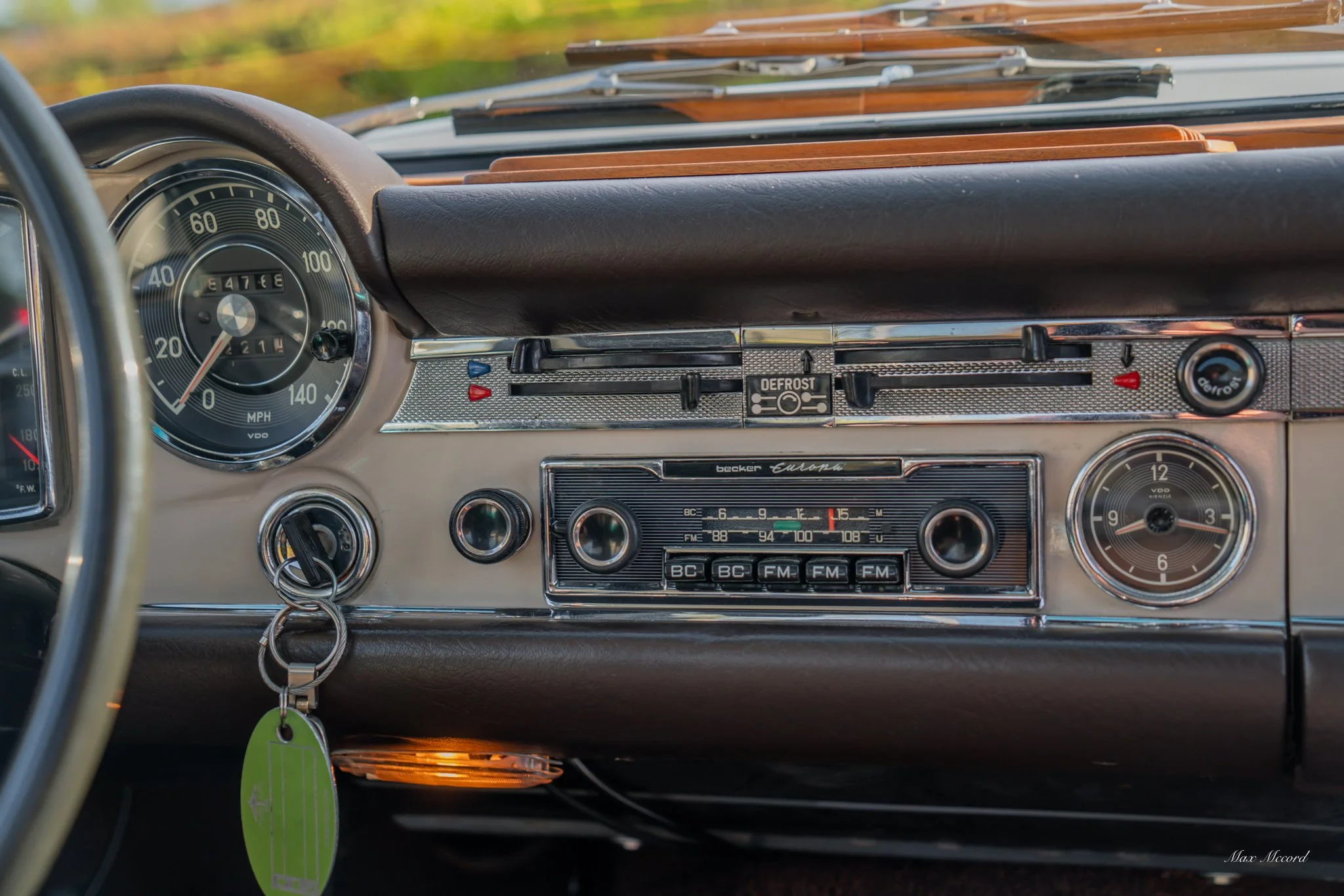 Dashboard of a vintage BMW car with a speedometer, radio, clock, key in ignition, and control switches.