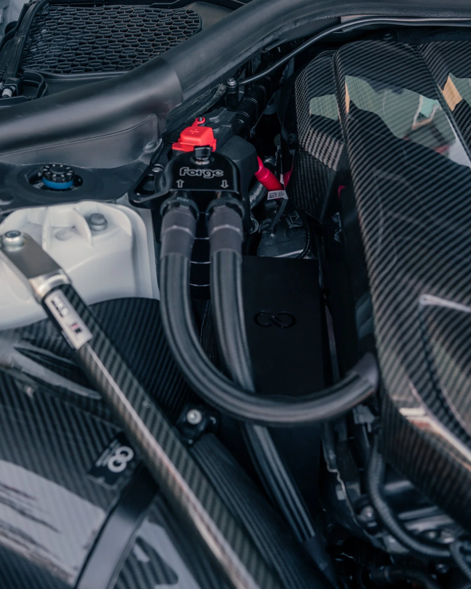 Close-up of a car engine with carbon fiber components and a Forge racing fuel system with silicone hoses and red fittings.