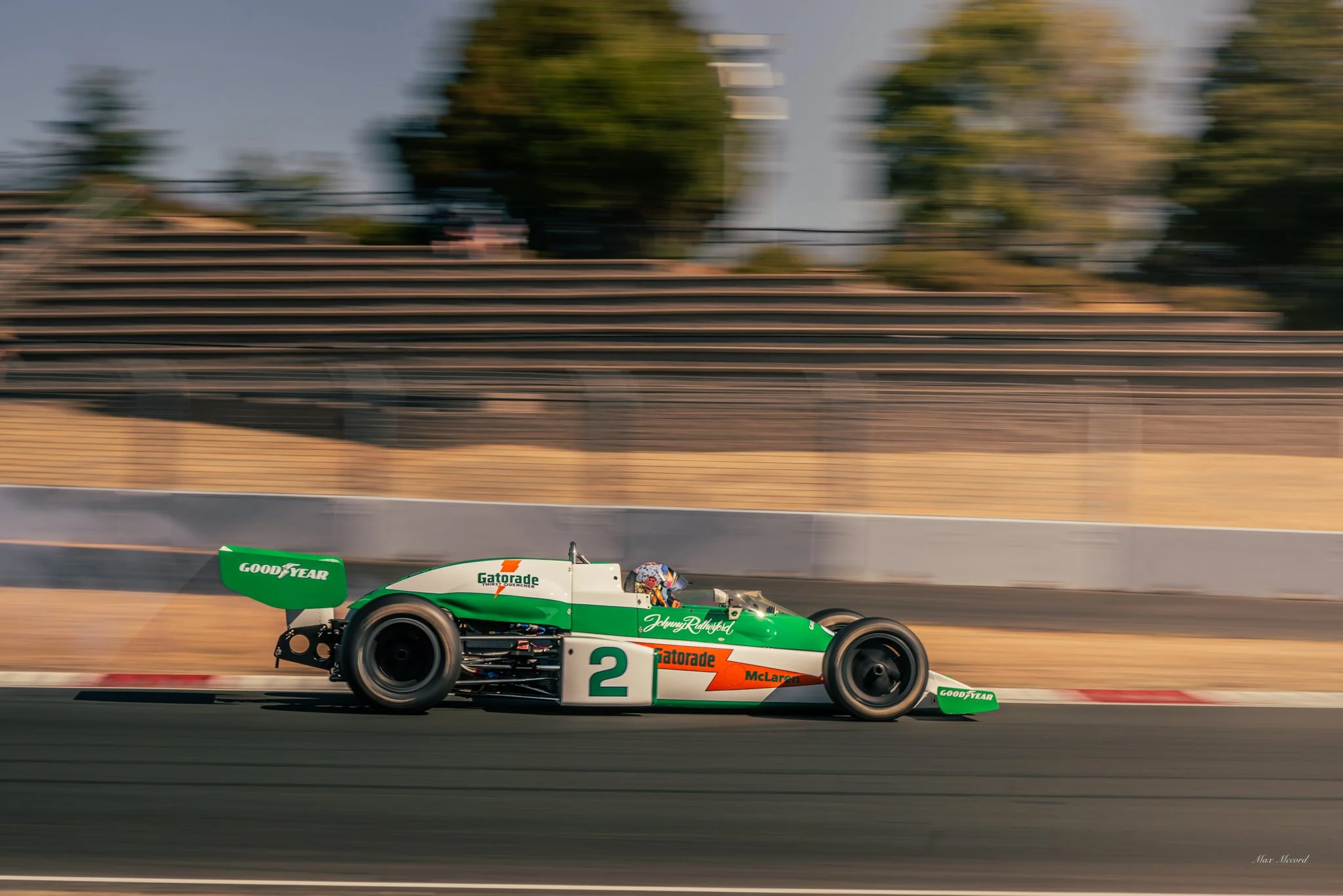 A vintage Formula 1 race car speeding on a racetrack with a blurred background, featuring green, white, and orange colors, sponsored by Gatorade and Goodyear.