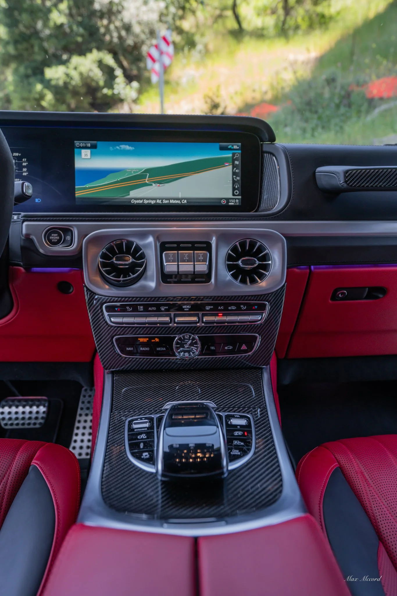 The interior of a luxury car showing a dashboard with a navigation screen displaying a map, climate controls, and red leather seats.