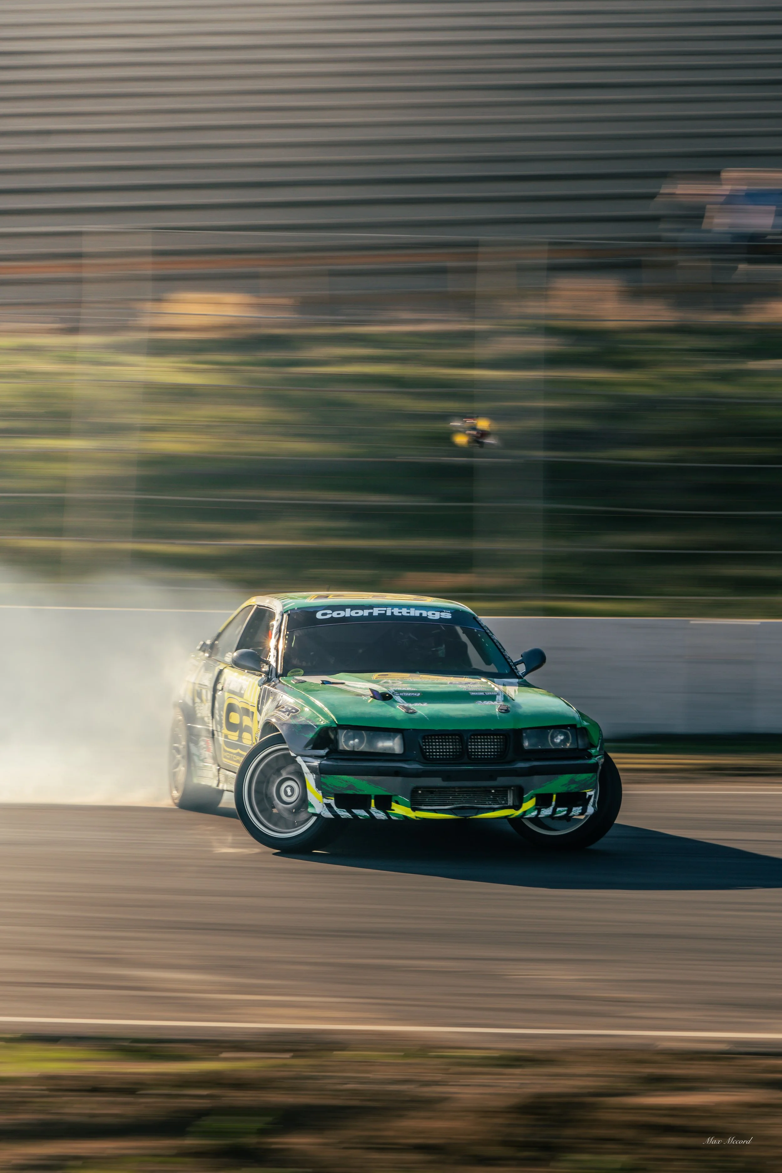 Green race car drifting on a track, creating smoke with a blurred background.