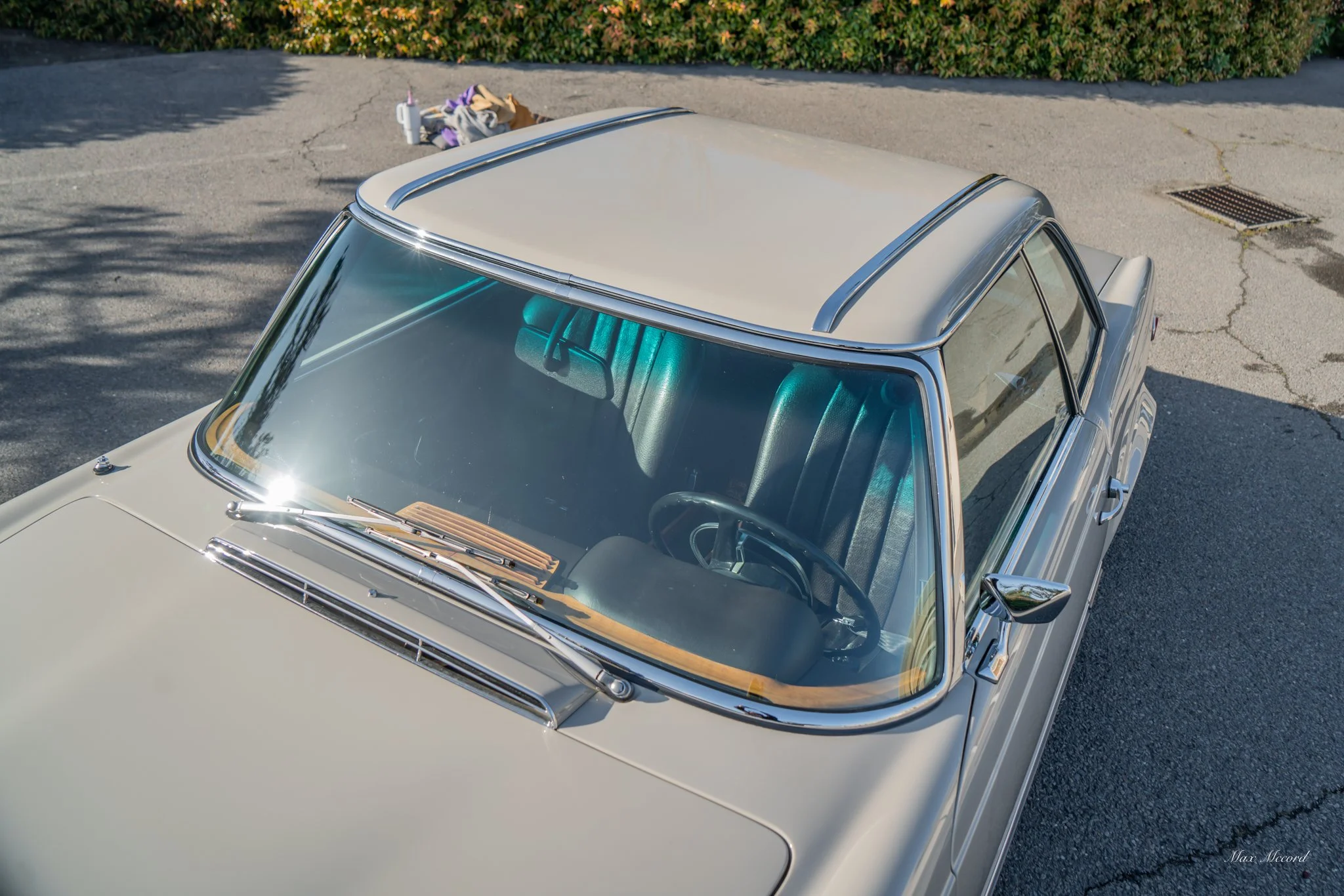 Top aerial view of a vintage beige car parked on a cracked asphalt surface with a pile of clothes and bags in the background.
