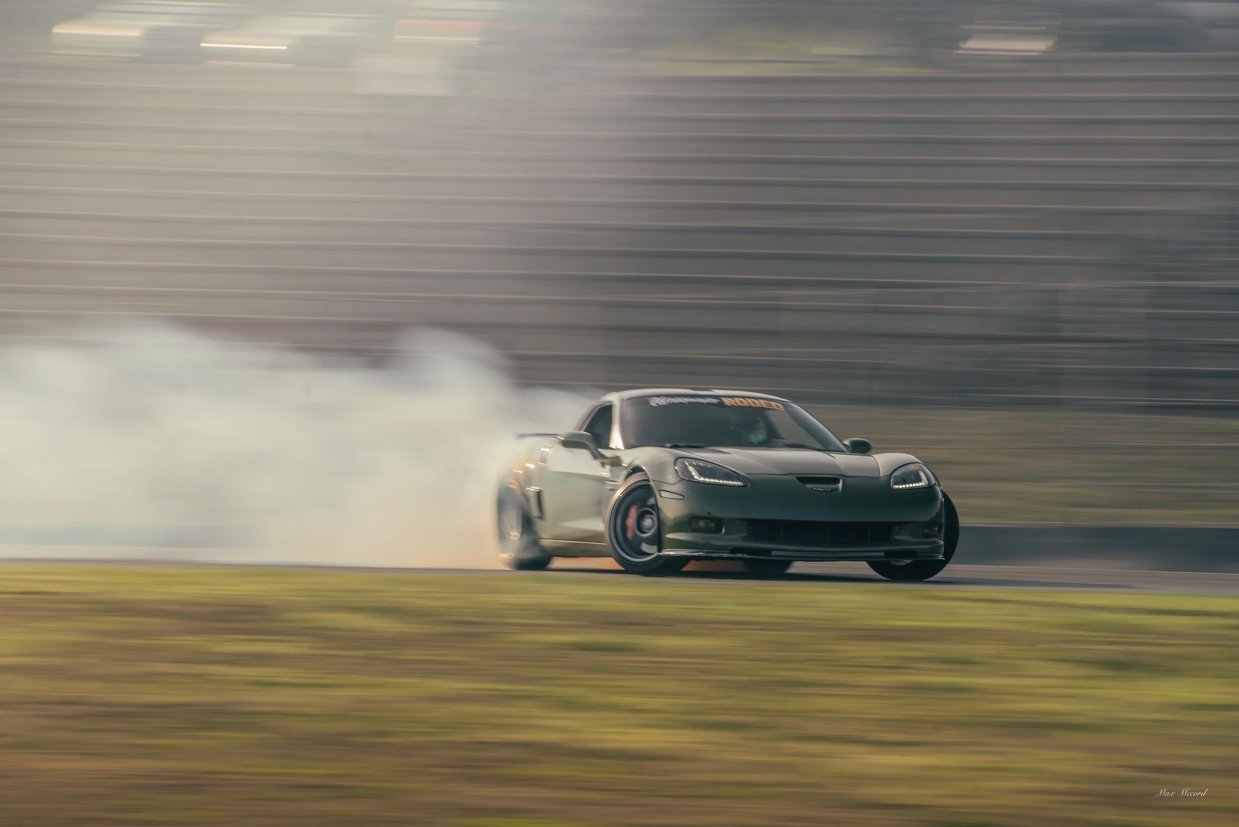 A black sports car drifting around a corner on a race track, producing smoke from the tires with a blurred background indicating high speed.