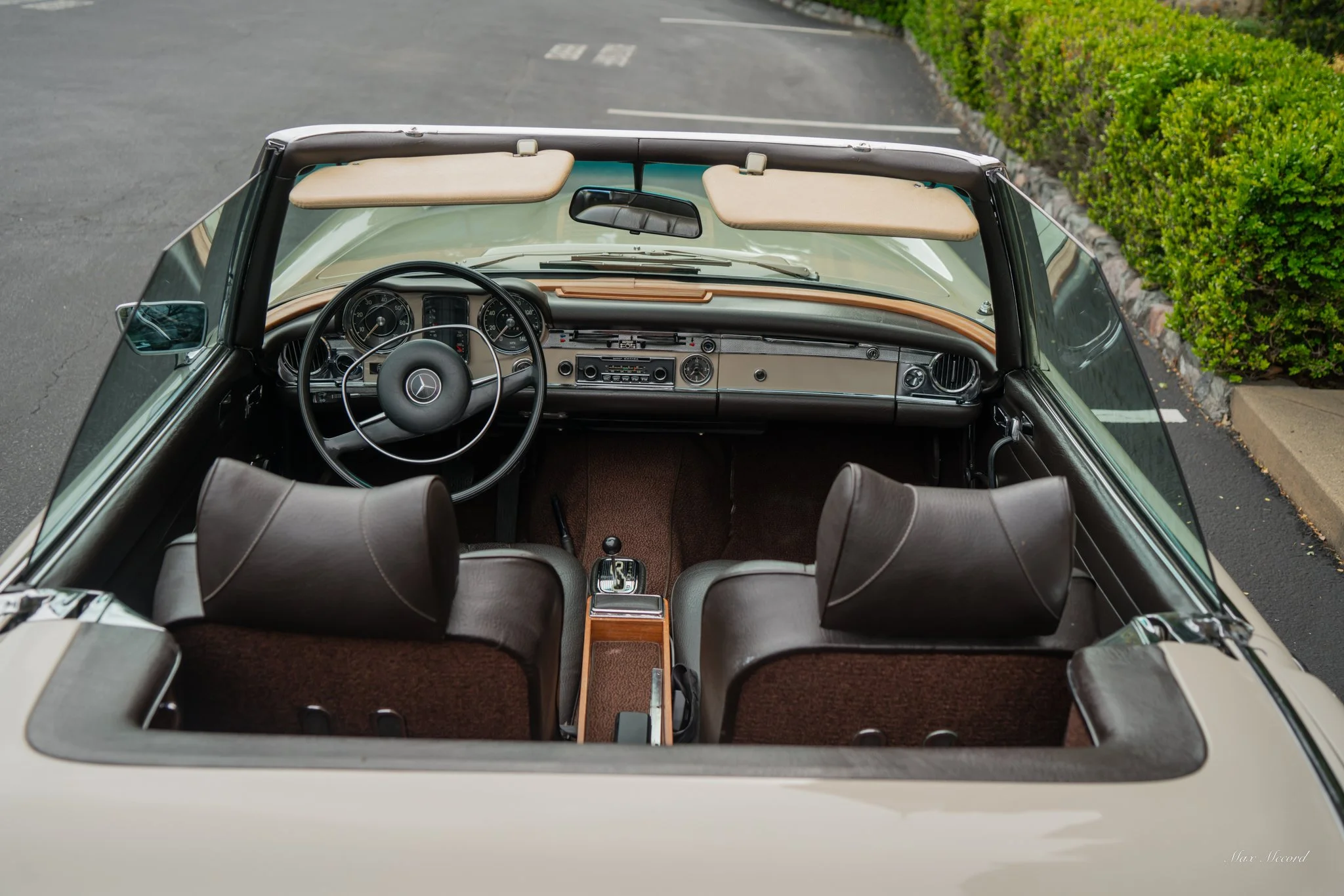 Interior view of a vintage convertible Mercedes-Benz car on a road, showing the dashboard, steering wheel, and front seats.