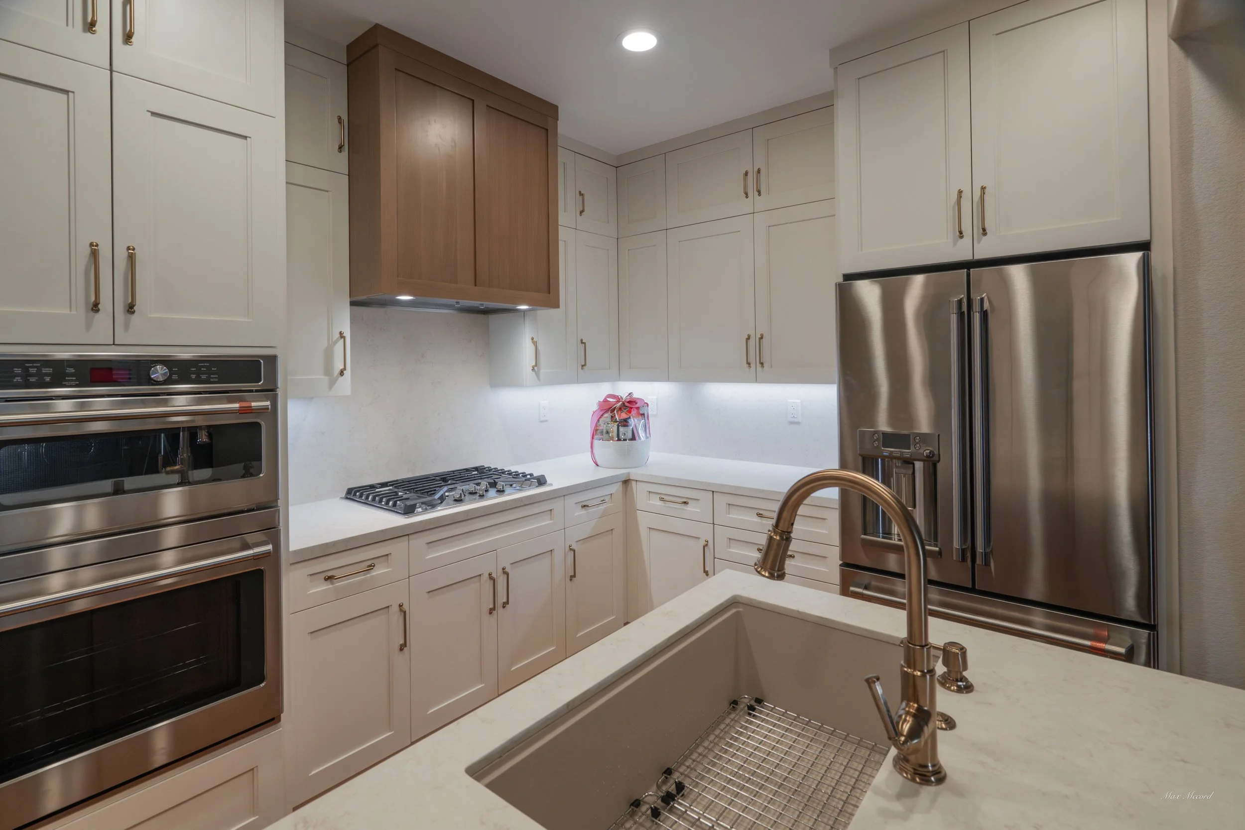 Modern kitchen with white cabinets, stainless steel appliances, a built-in oven and microwave, a gas stove, and a double-door refrigerator. There is a white countertop with a sink and a gold faucet.