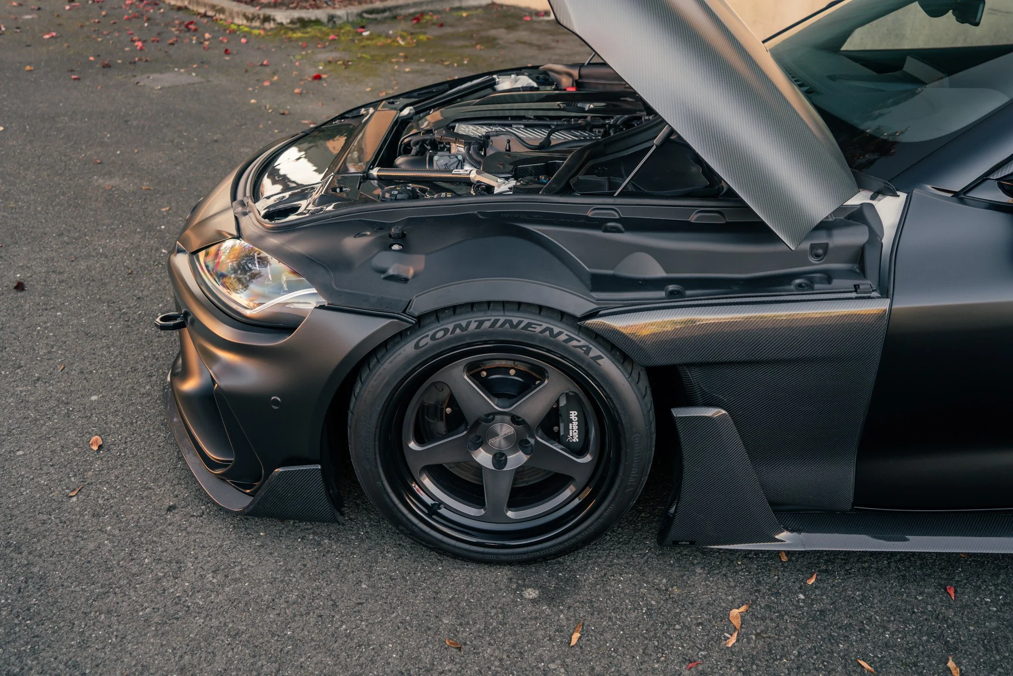 Front view of a black sports car with the hood open, showing the engine.