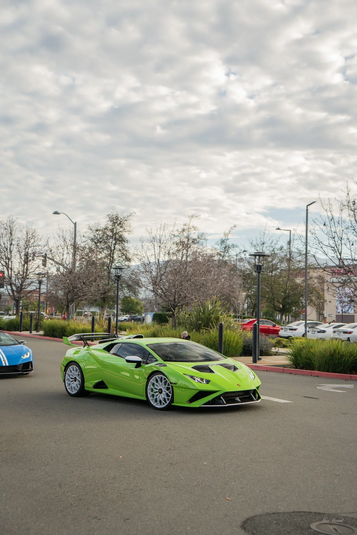 A bright green Lamborghini sports car parked on the street amid other cars with a cloudy sky overhead.
