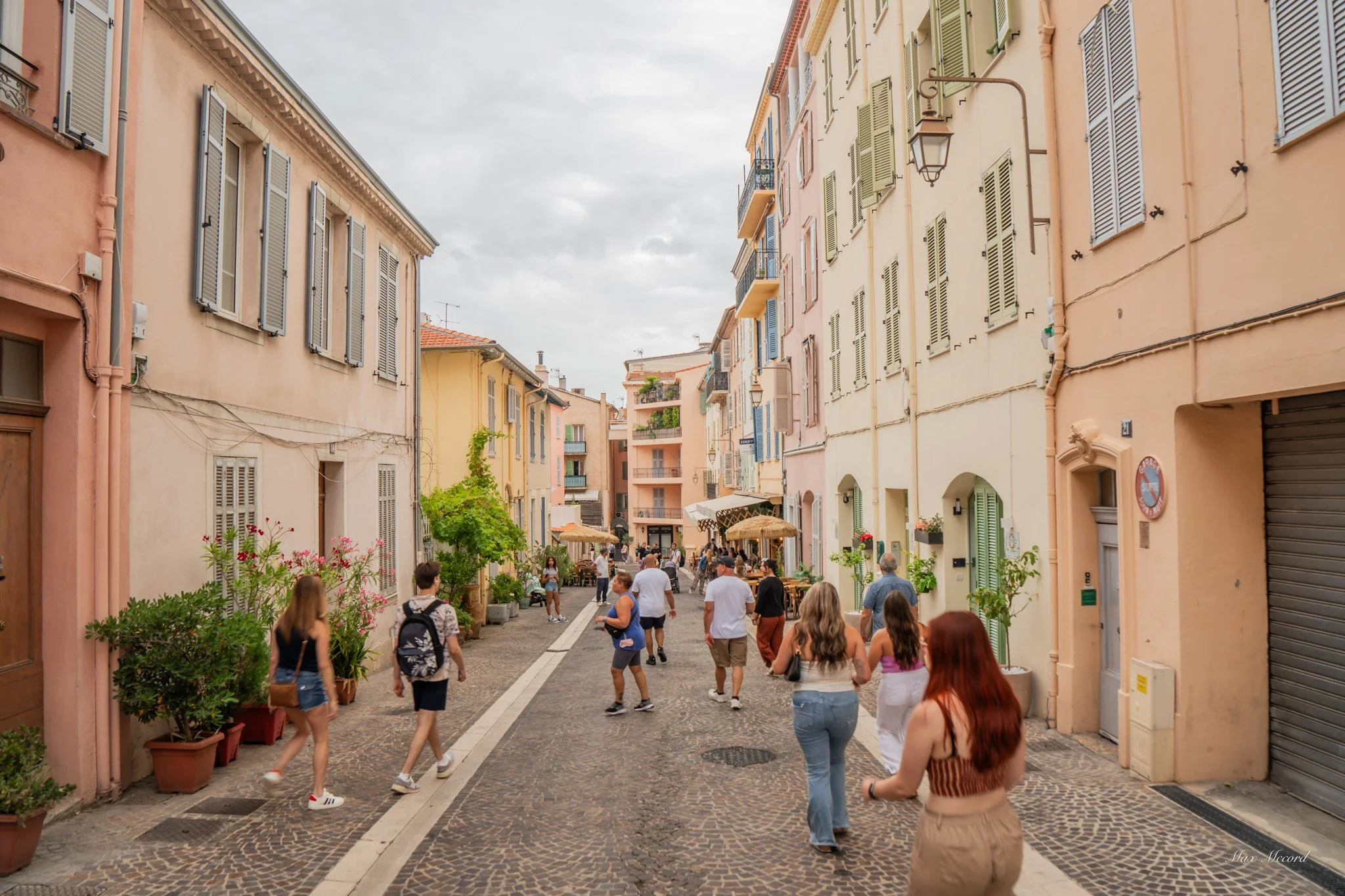 People walking on a cobblestone street lined with pastel-colored buildings and outdoor cafes in a European city.