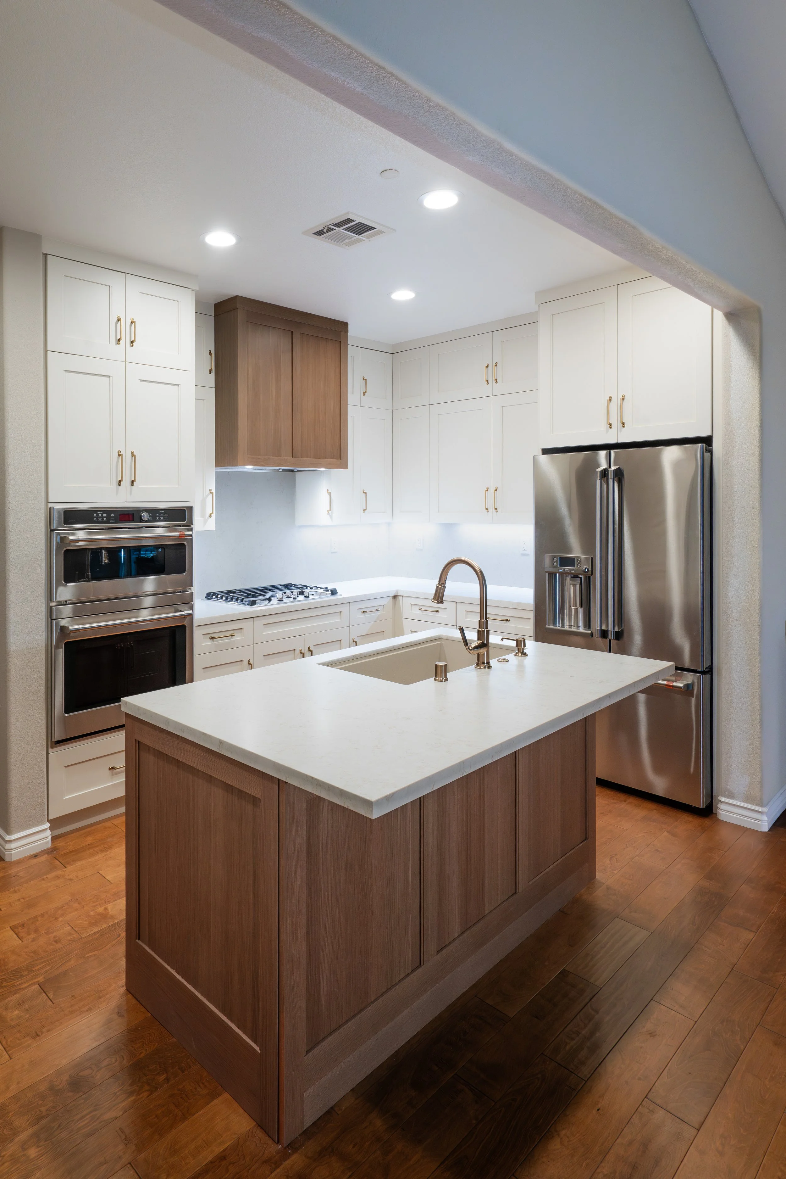 Modern kitchen with white cabinets, stainless steel appliances, wooden accents, and a kitchen island with a sink.