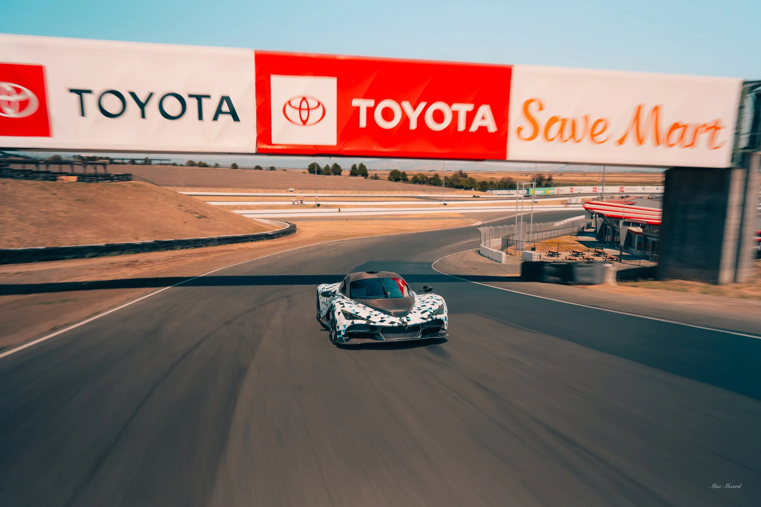 A sports car on a race track passing under a large Toyota billboard.