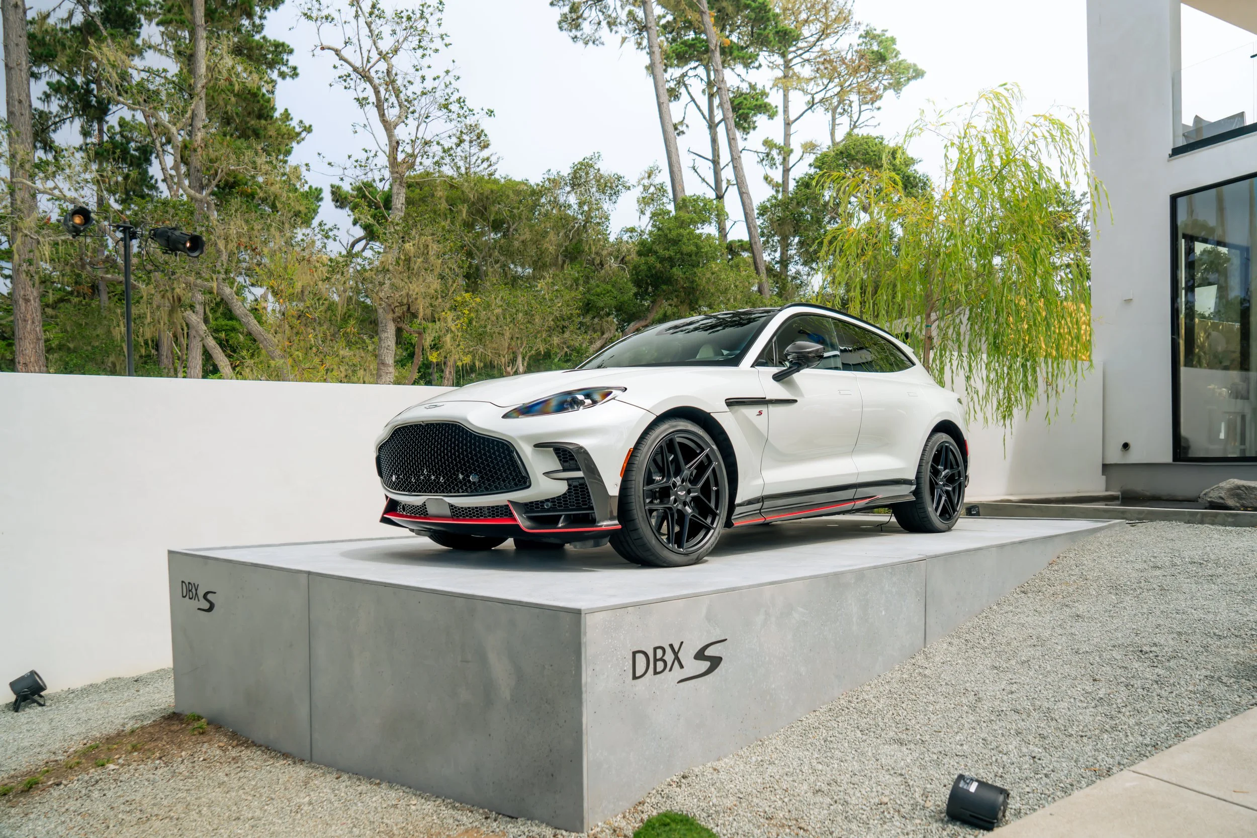 A white sports car, the Subaru BRZ S, displayed outdoors on a concrete platform with trees and a modern building in the background.