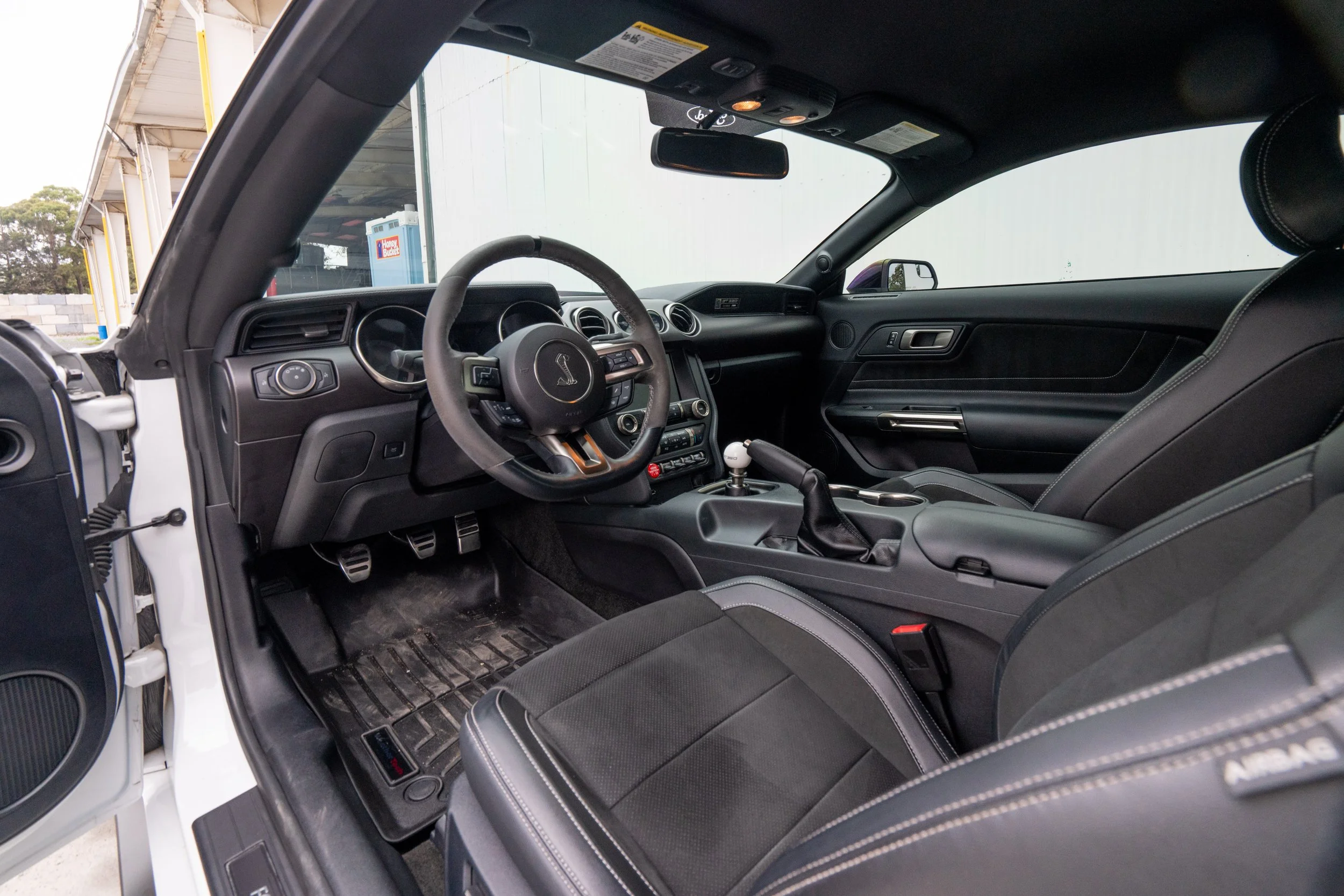 Interior of a Shelby car, showing the steering wheel, gear shifter, and black leather seats.