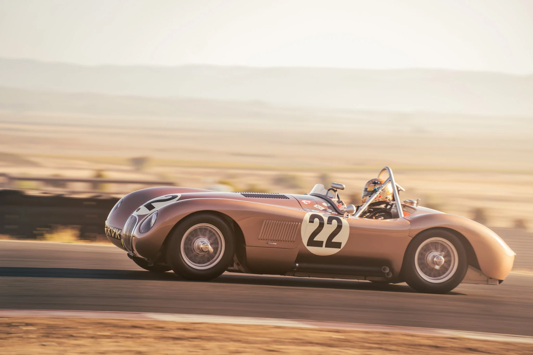 A vintage race car, number 22, speeding on a racetrack in a desert landscape during sunset.