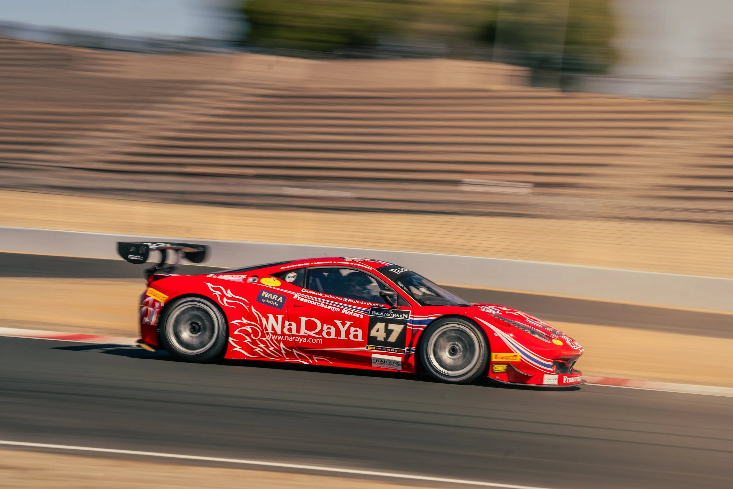 A red race car with racing decals and the number 47 on the side, speeding on a race track with a blurred background.