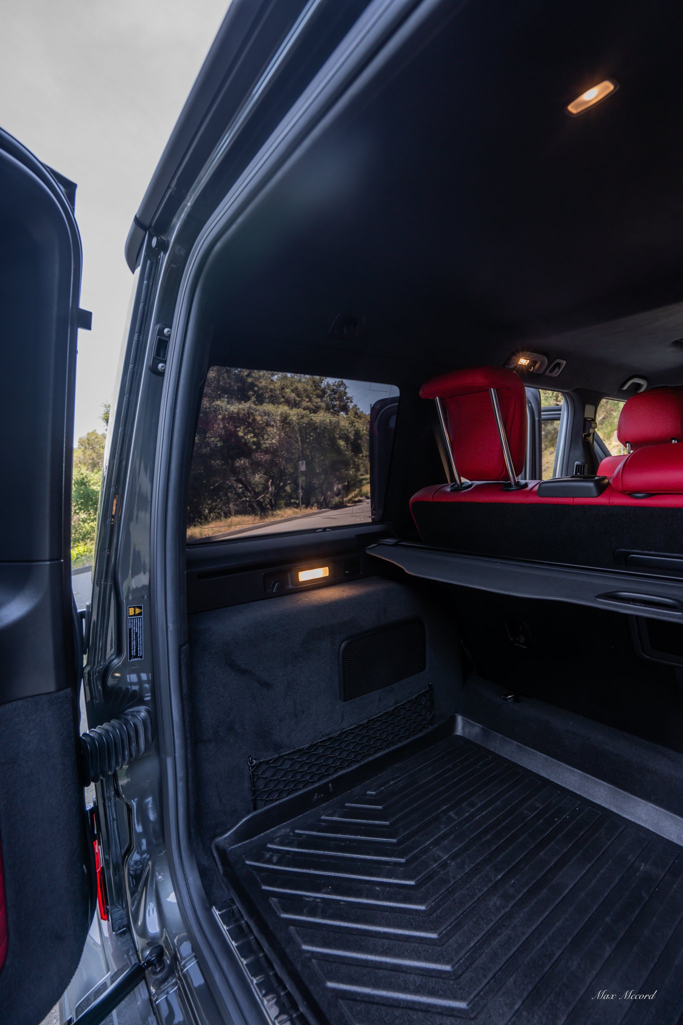 Interior of an SUV showing the back hatch area, red headrests on the seats, a window with trees outside, and a cargo mat on the floor.