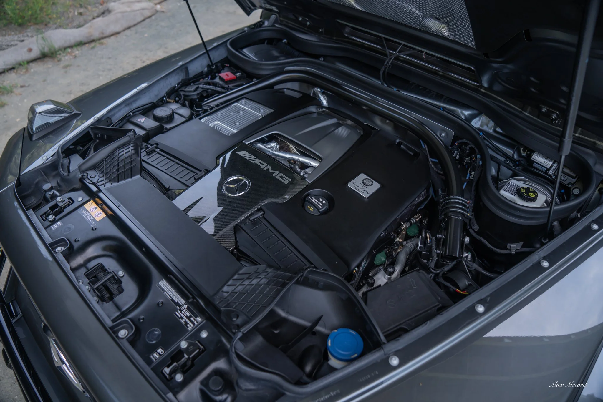 Close-up of a Mercedes-Benz AMG V8 engine under the hood, with black engine cover and various components visible.