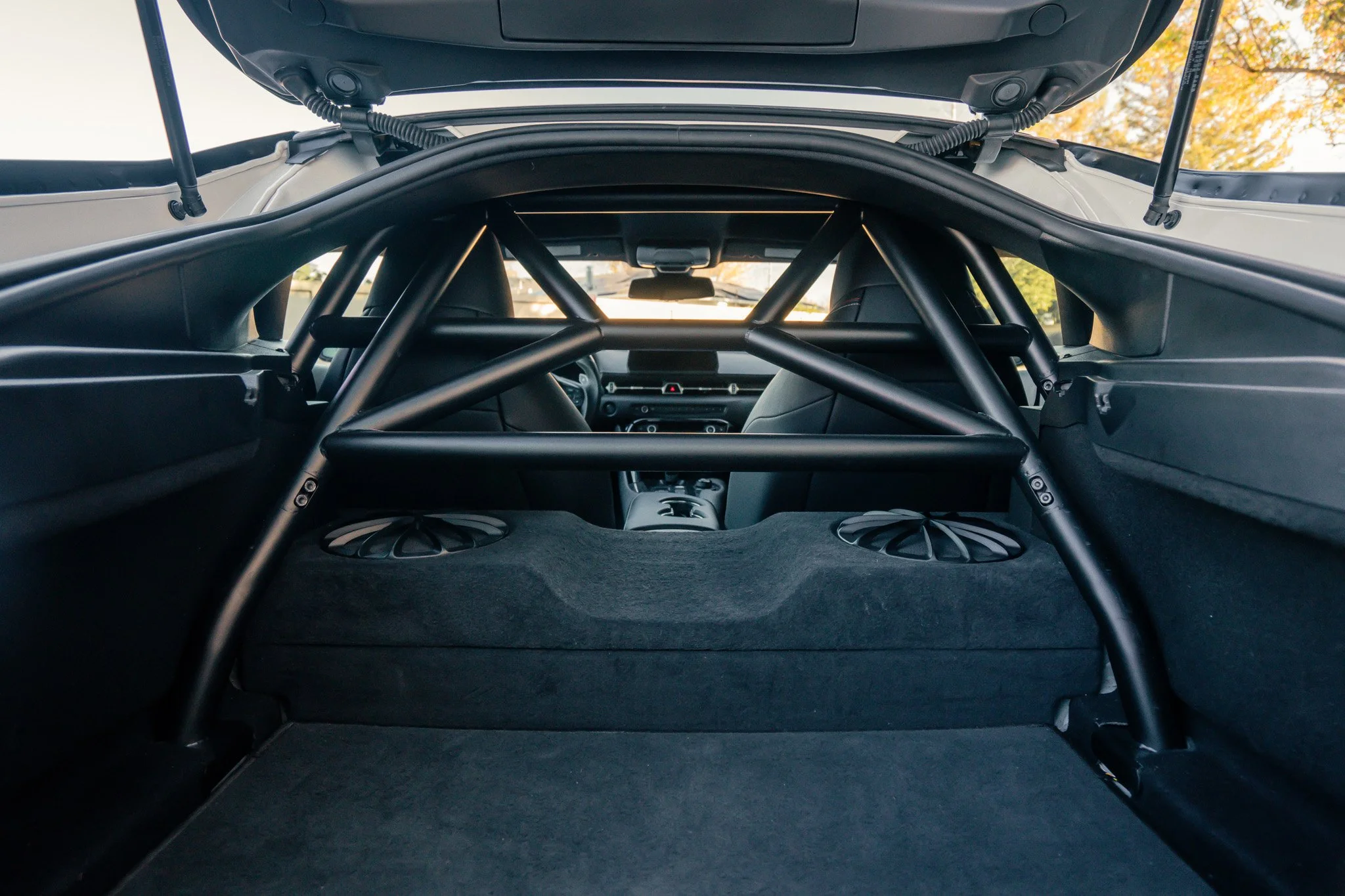 View from the back of a race car's interior showing a roll cage, rear seats, and a dashboard with the steering wheel visible.