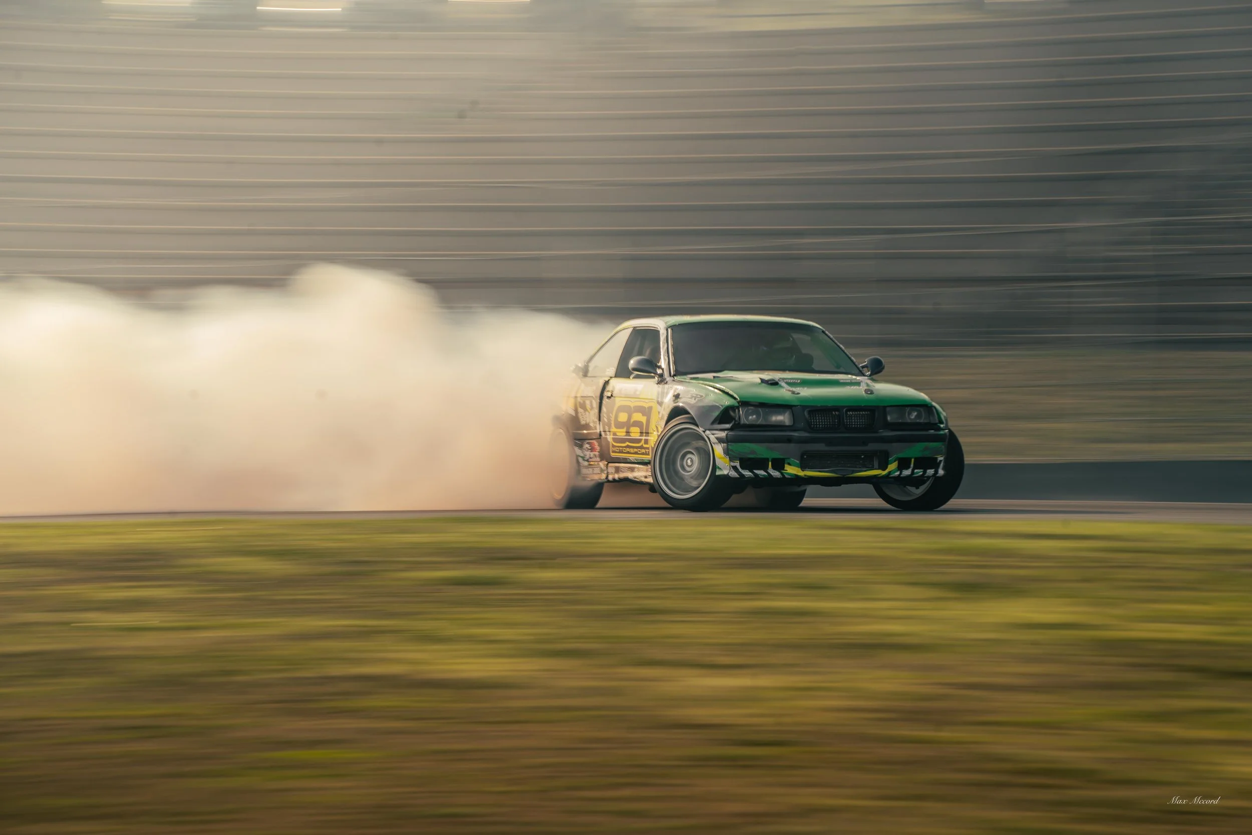 A green race car drifting on a track, with smoke billowing from its tires.