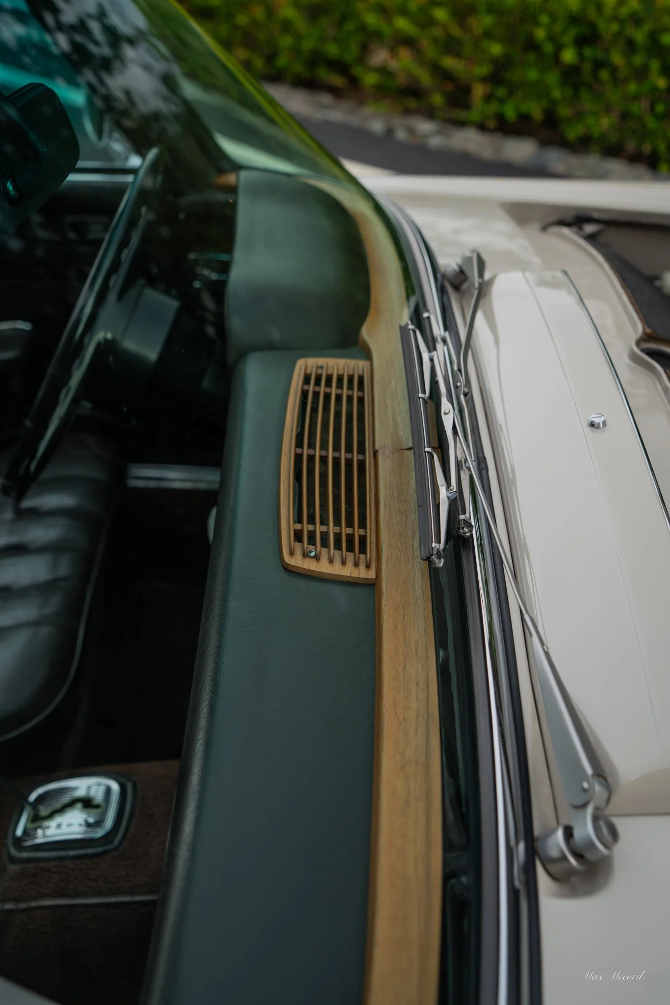 Close-up of the dashboard and windshield of a vintage car with a wooden panel and black interior.
