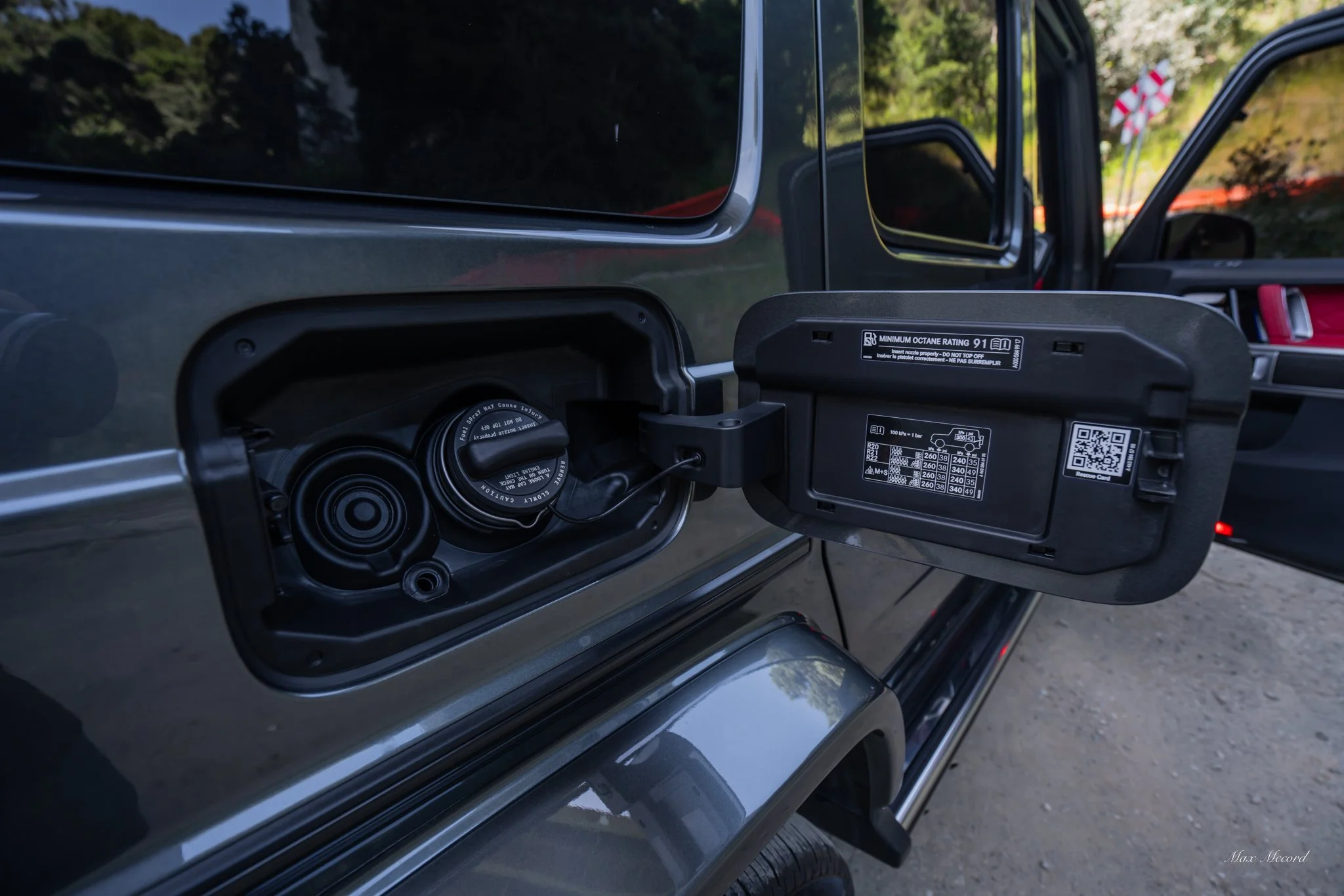 Open fuel cap of a vehicle showing fuel nozzle and inside of fuel tank with information label on fuel door.